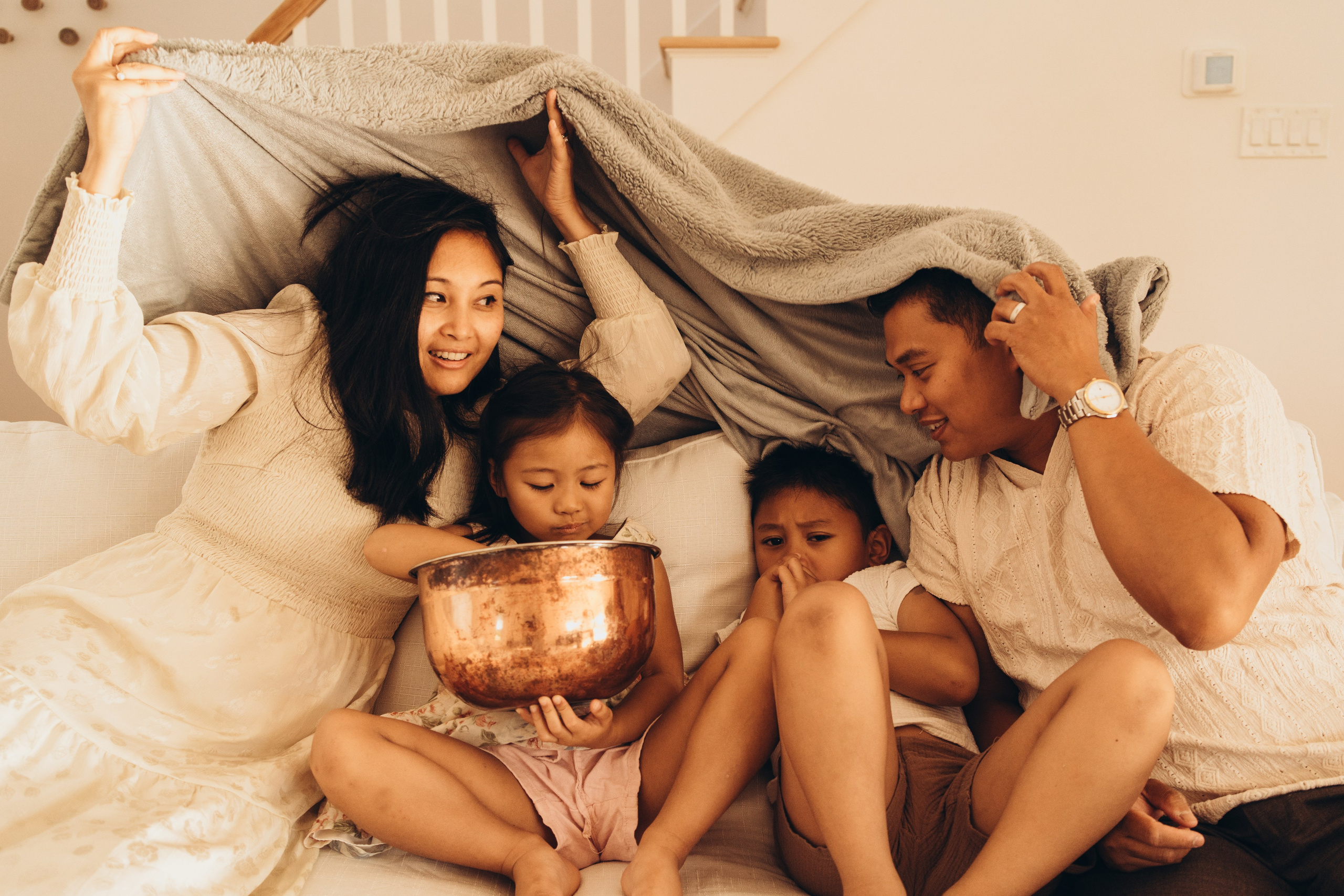 Parents and children hiding under a blanket on the bed, laughing