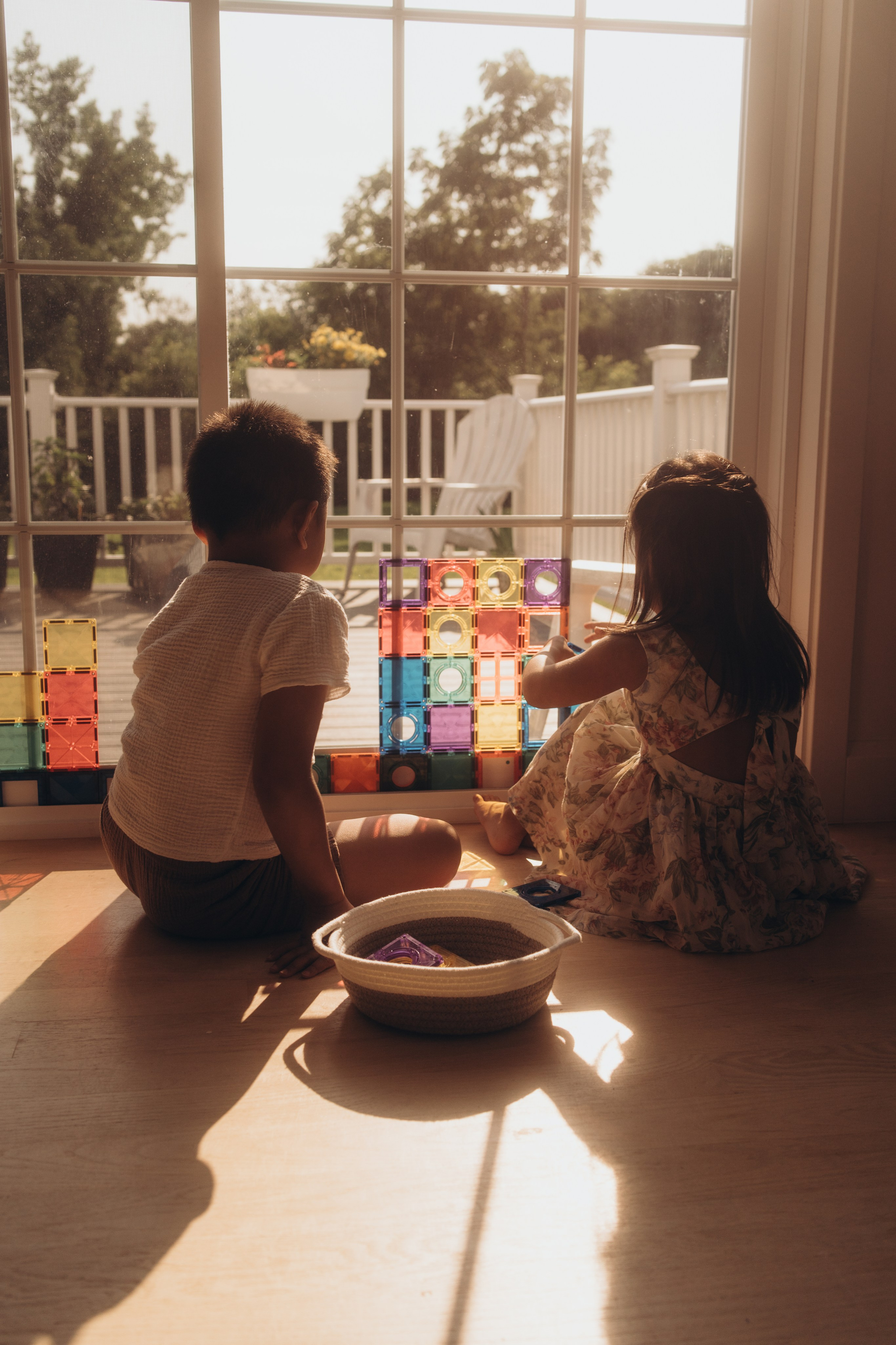 Brother and sister playing with colorful building tiles by a sunny window