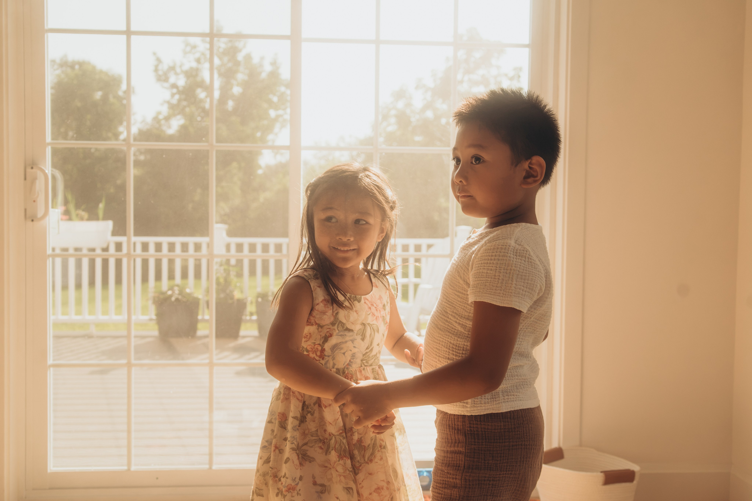 Brother and sister holding hands and dancing by the window 