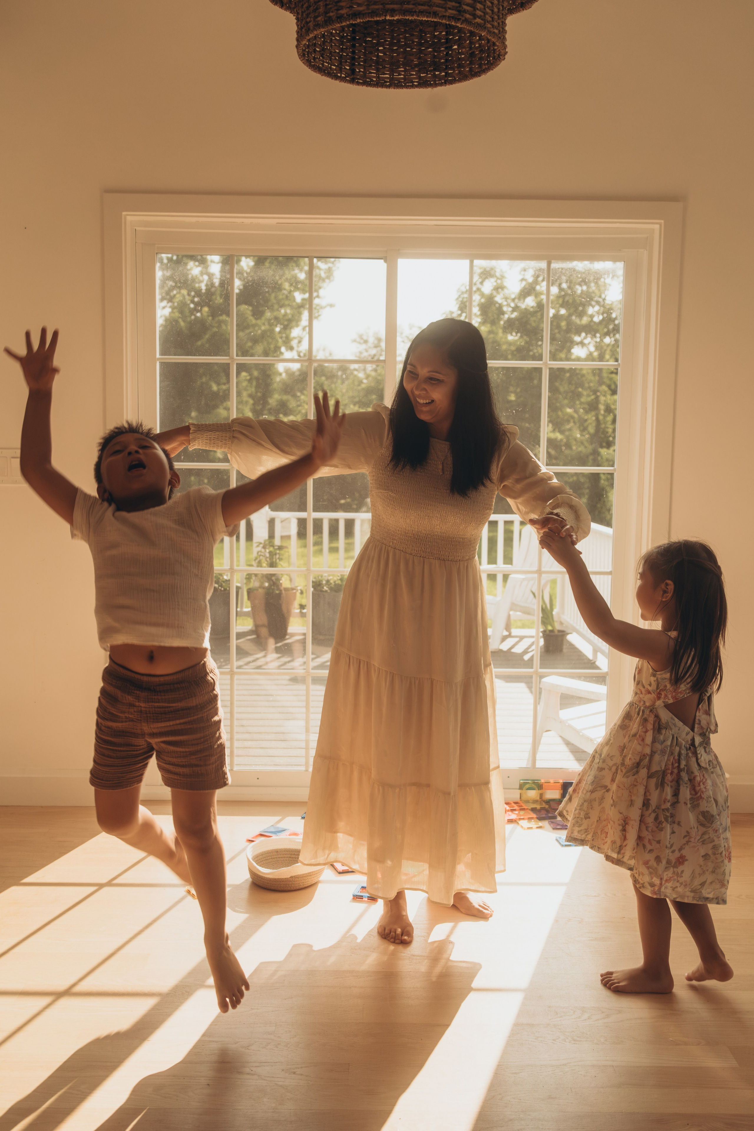Mother dancing with her son and daughter by the window, arms in the air