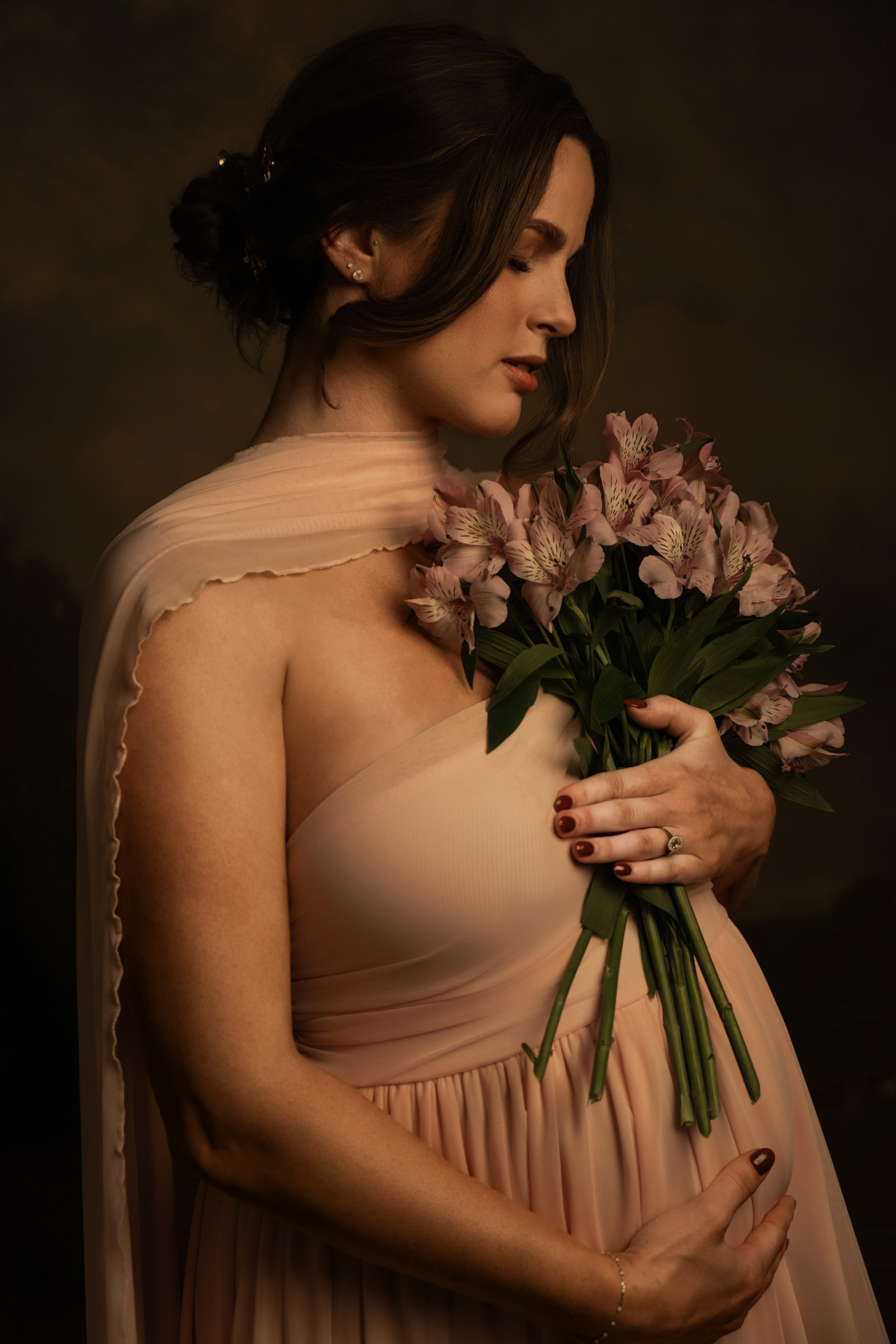 Pregnant woman holding pink blooms, looking down, warm painterly light