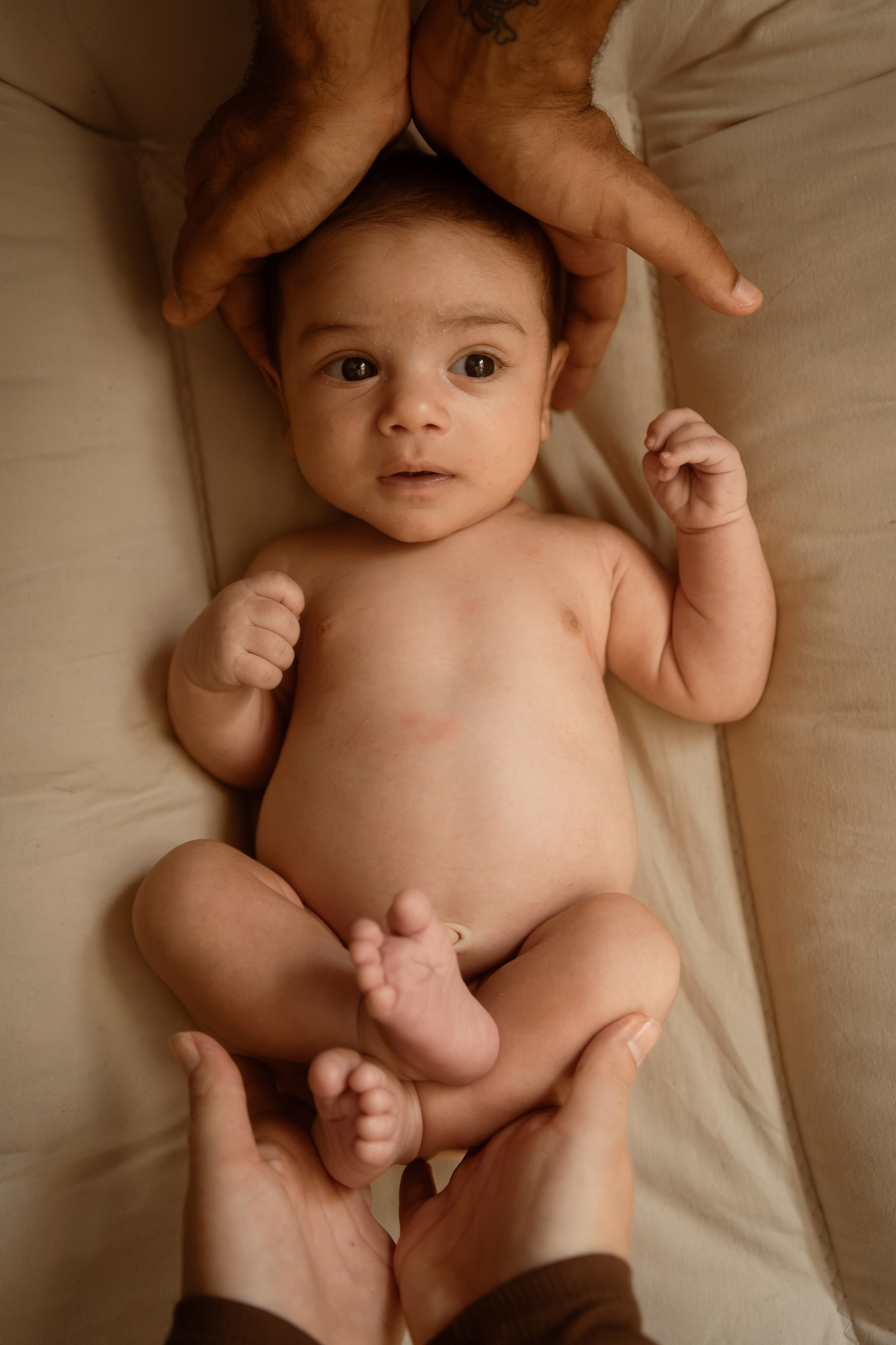 Newborn on a blanket with a parent's hands cradling their head