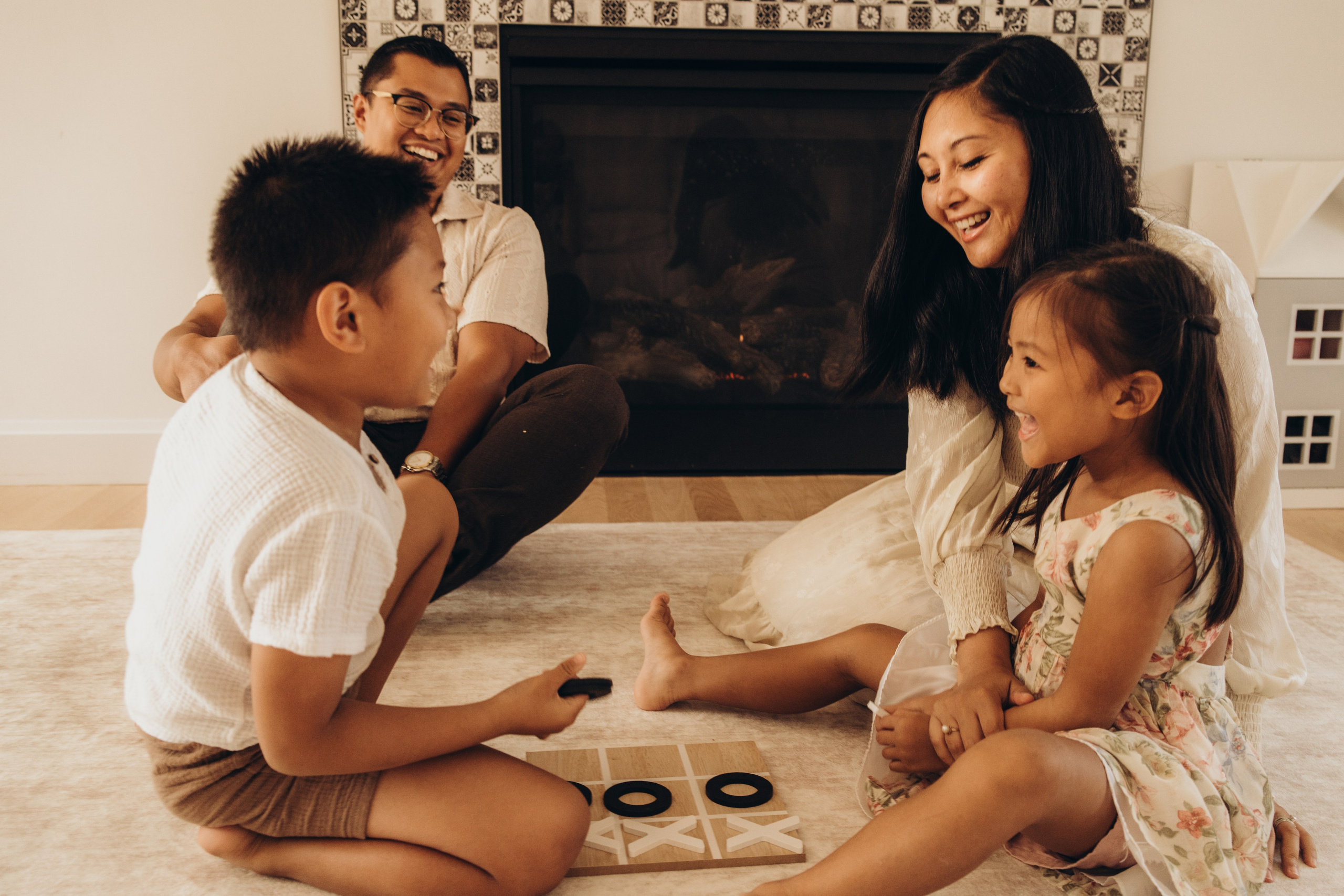 Family of four playing a board game on the living room floor by the fireplace, East Haddam CT