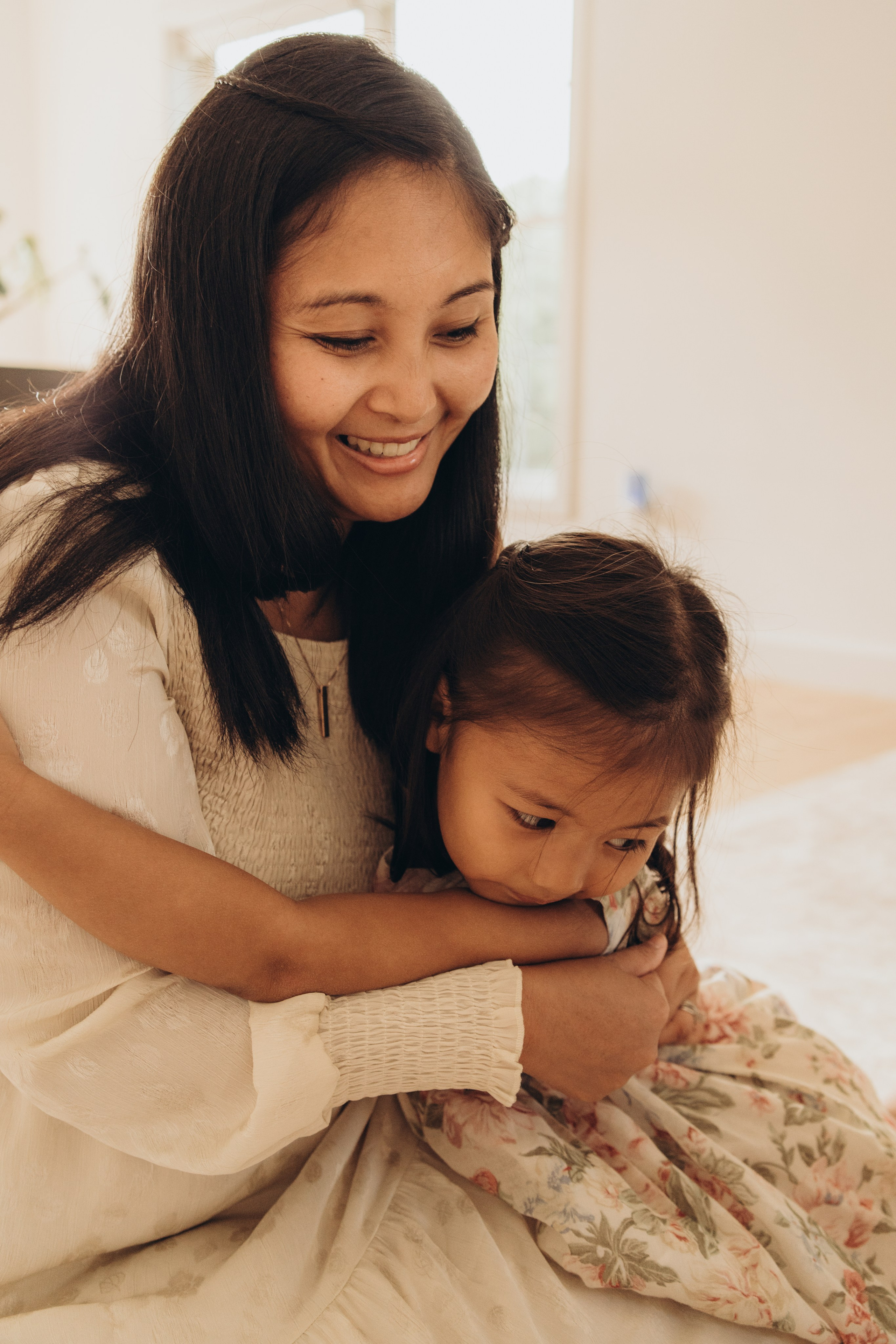 Mother hugging her daughter on the floor, both smiling