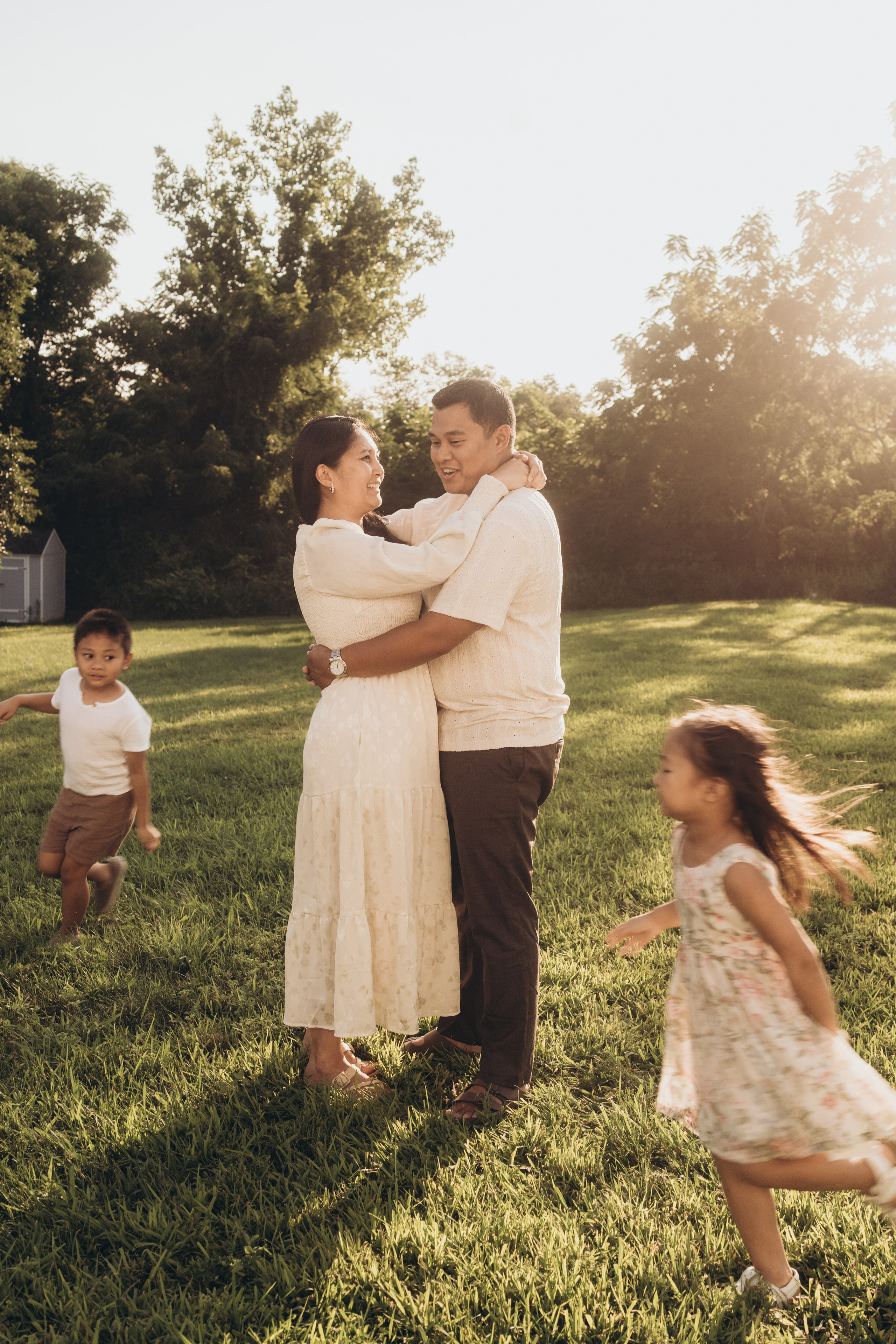 Parents embracing in the yard while their children run in the grass at sunset