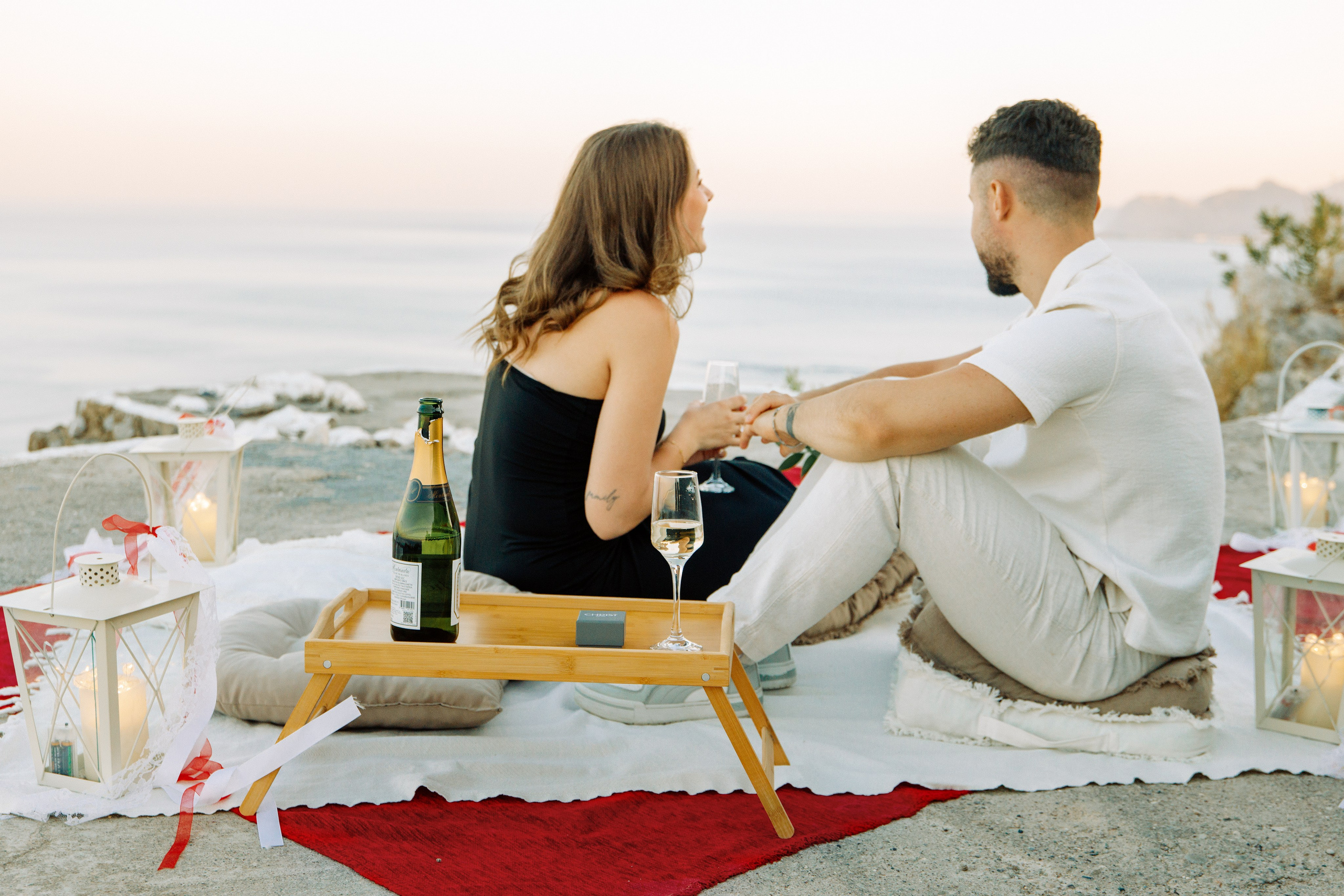 "Rückenansicht eines Paares, das nebeneinander auf den Felsen des Profitis Ilias sitzt. Sie schauen gemeinsam auf das tiefblaue Ägäische Meer und die Küste von Rhodos unter ihnen. Ein Moment des Innehaltens nach dem Heiratsantrag in der friedlichen Natur Griechenlands."
