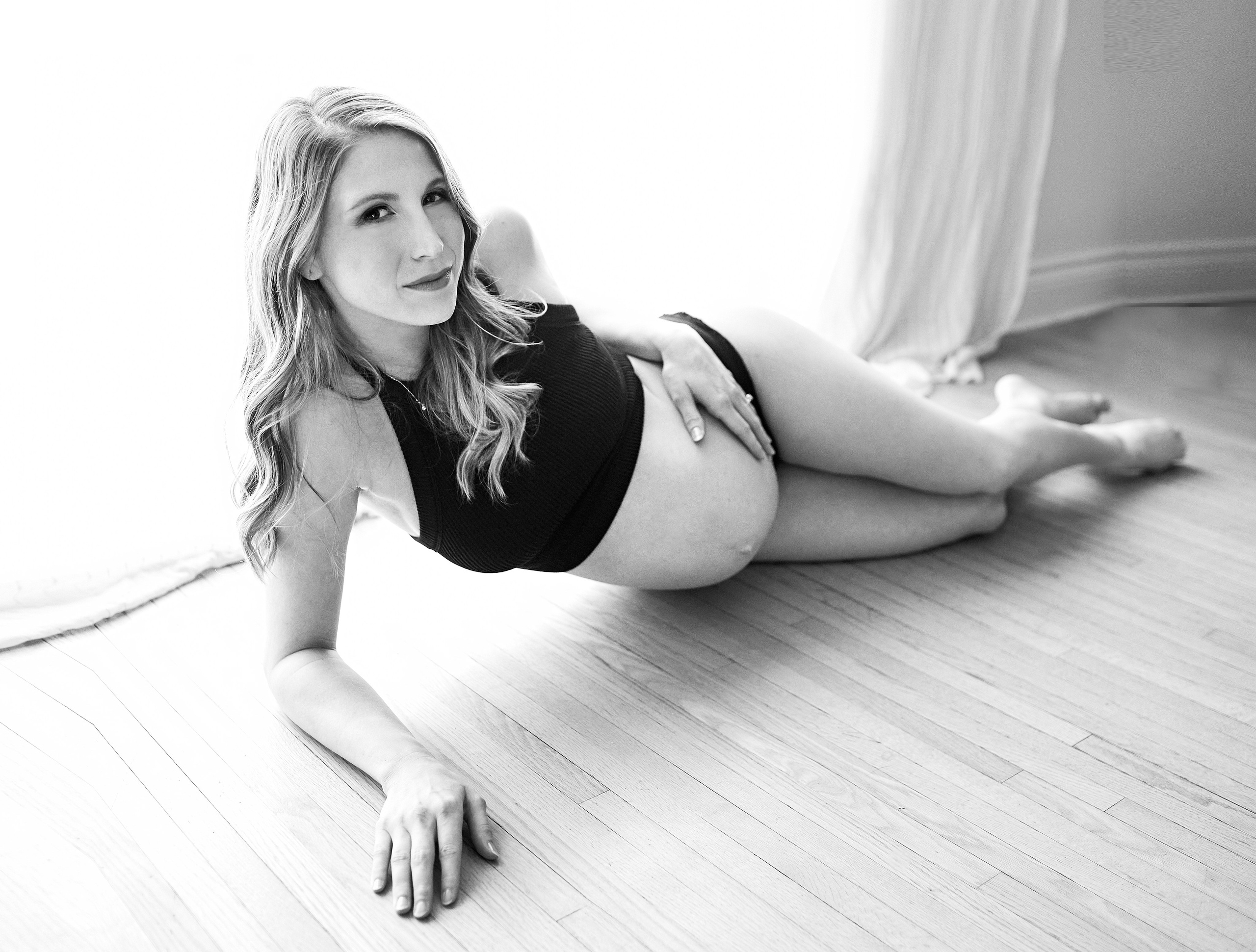MATERNITY PHOTO OF WOMAN LAYING ON GROUND LOOKING UP AT CAMERA WITH BARE PREGNANT STOMACH 