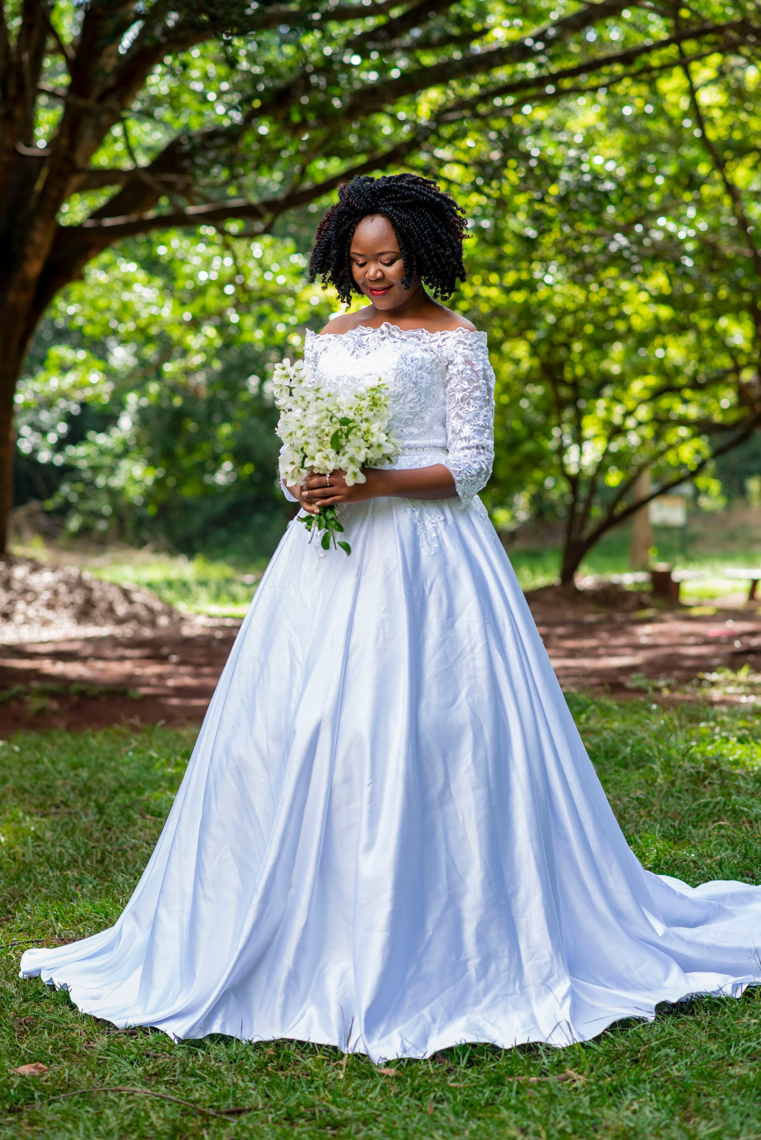 A full portrait of a bride holding a bouquet in a lush green park during a wedding photo session in Nairobi's Arboretum