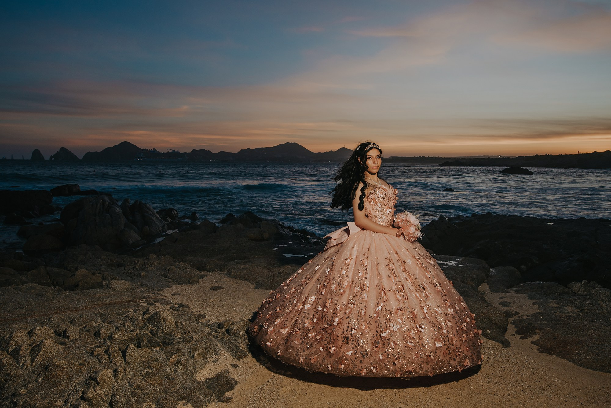 Quinceañera wearing an elegant gown during a sunset beach photoshoot in Los Cabos, Mexico