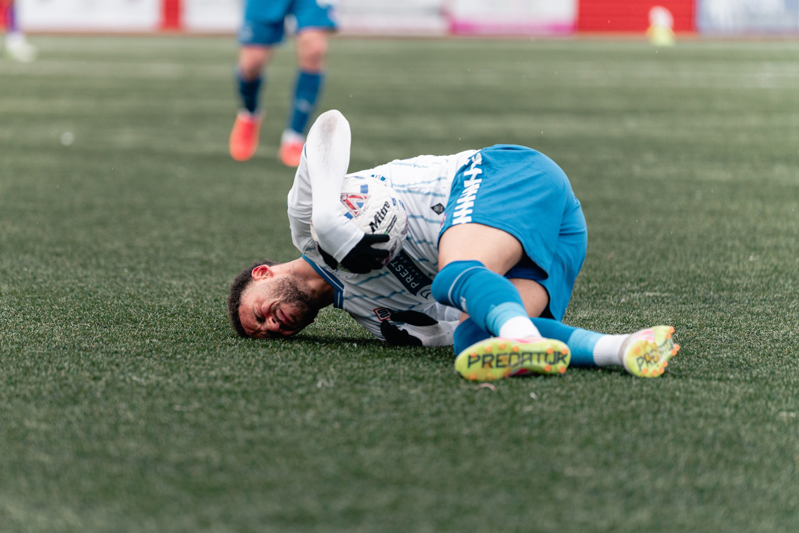 Reiss McNally lies on the pitch clutching the ball after going down during Tamworth vs Hartlepool at The Lamb Ground.