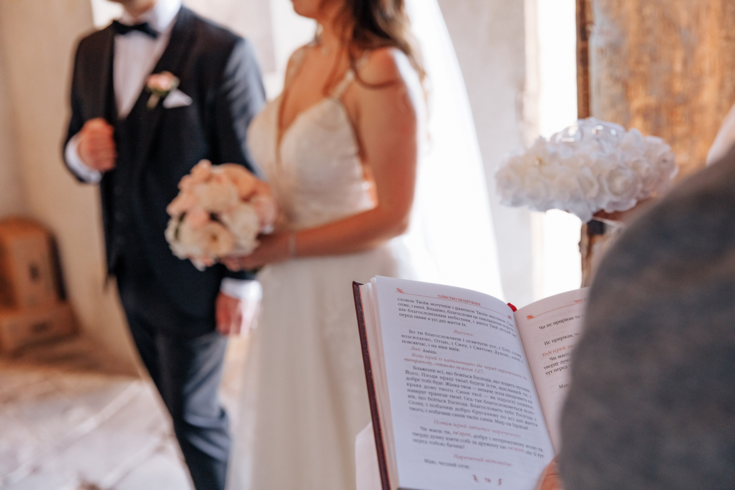 Ein Gebetbuch in ukrainischer Sprache auf dem Hintergrund des Brautpaars, ein symbolischer Moment während der Hochzeitszeremonie.