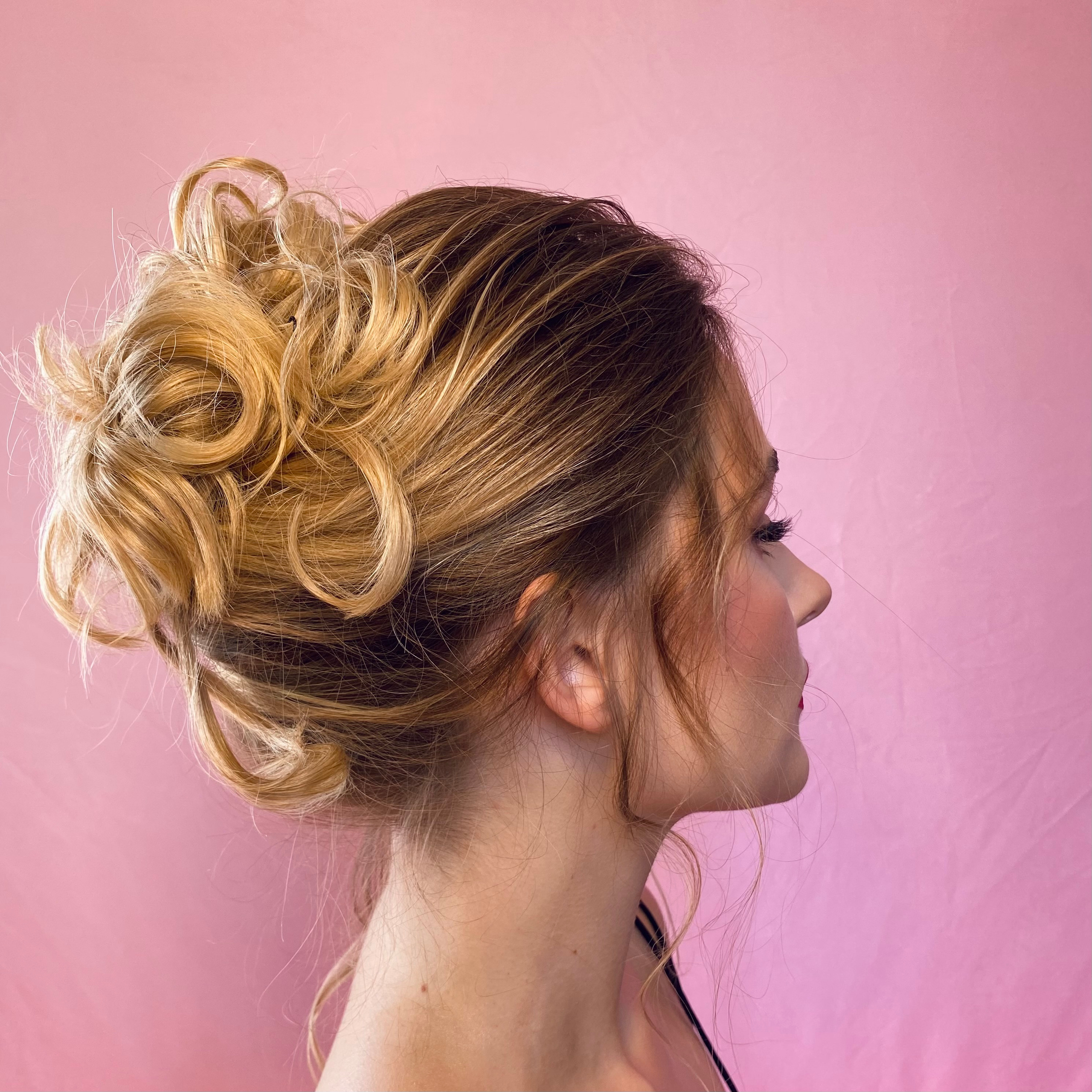 white skinned girl with blue eyes, dewy makeup and romantic up-do hairstyle on a pink background