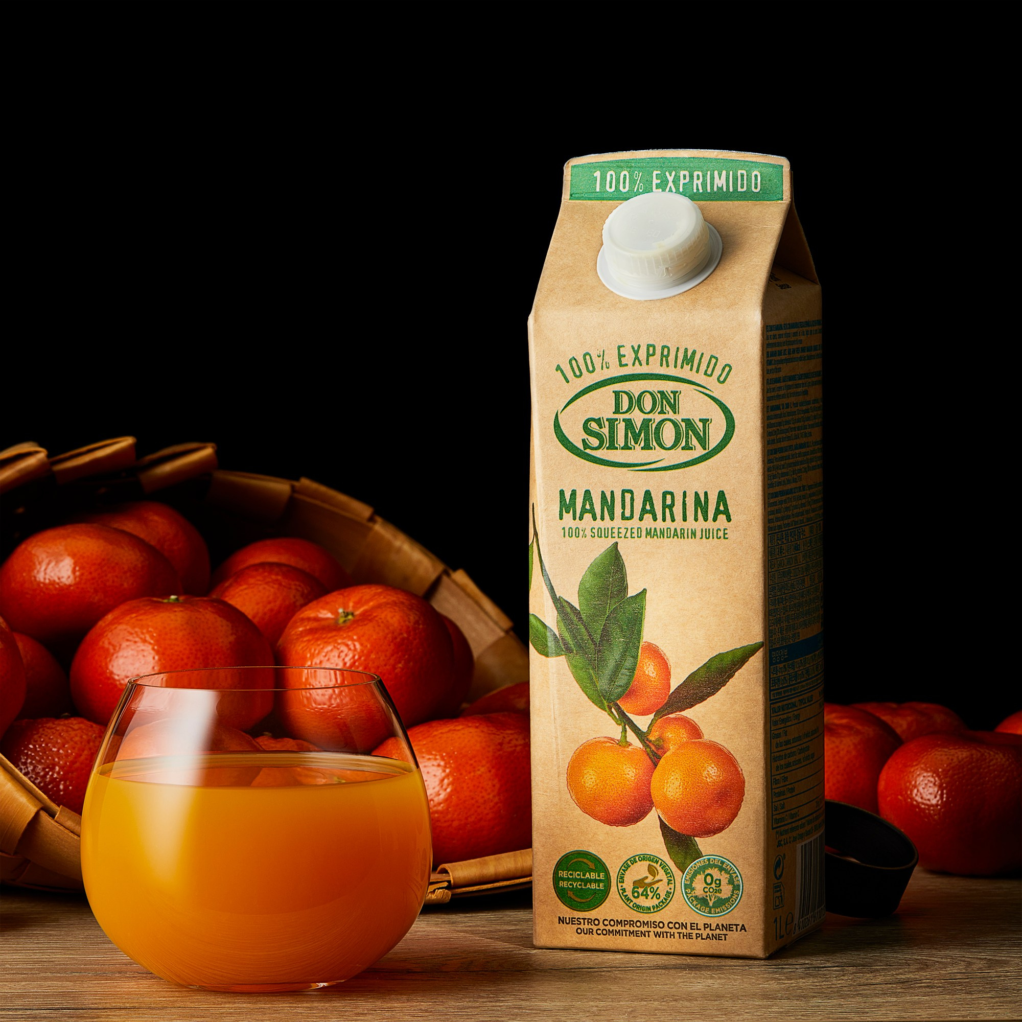 Photographer Roman Djuzev - The photograph shows Don Simon brand mandarin juice poured into a transparent glass, with a juice carton placed next to it. Behind the glass and the carton, part of a basket with mandarins is visible, and the background is dark.