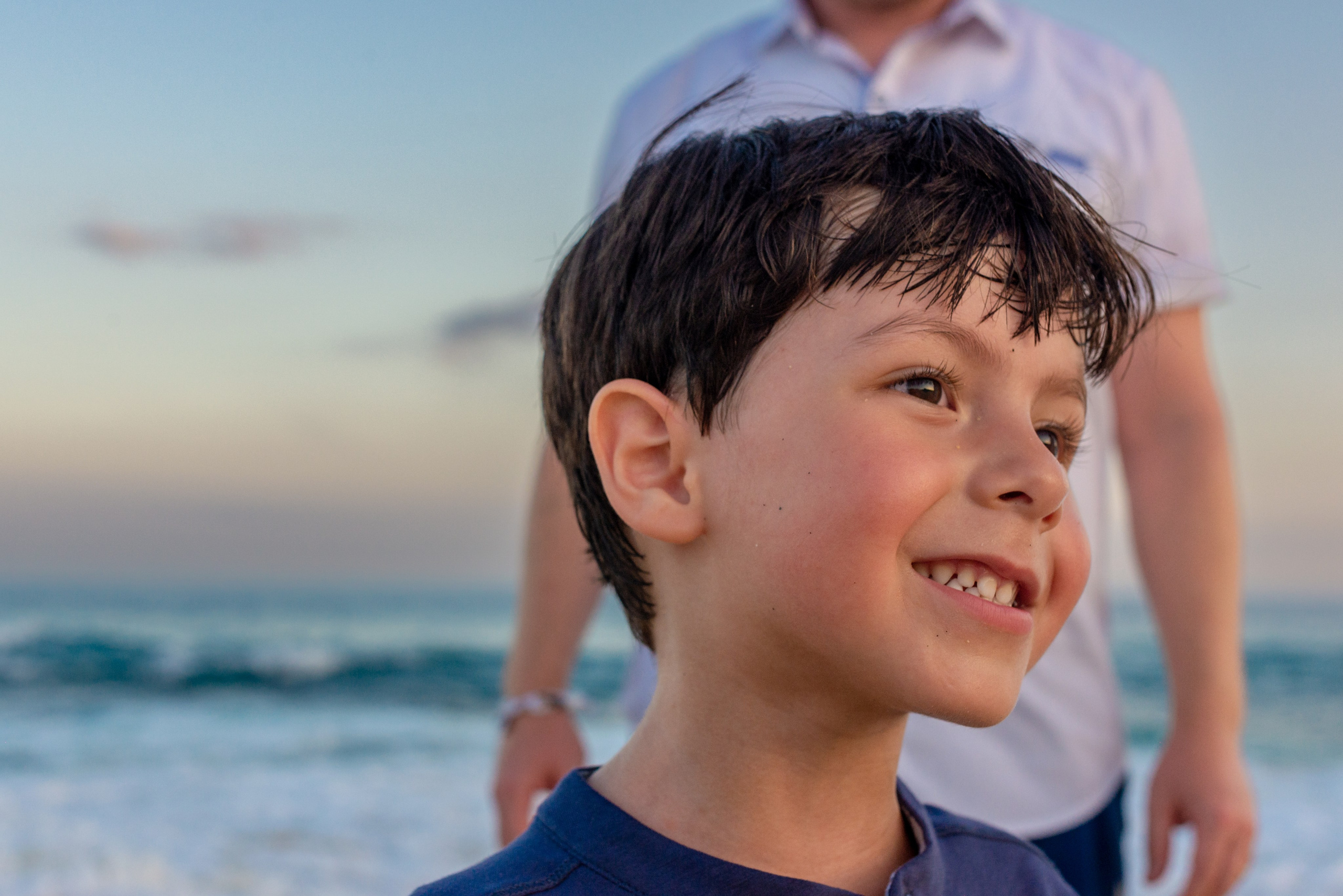 Candid child portrait in Los Cabos – smiling boy playing on the beach with ocean backdrop, natural family photography moment