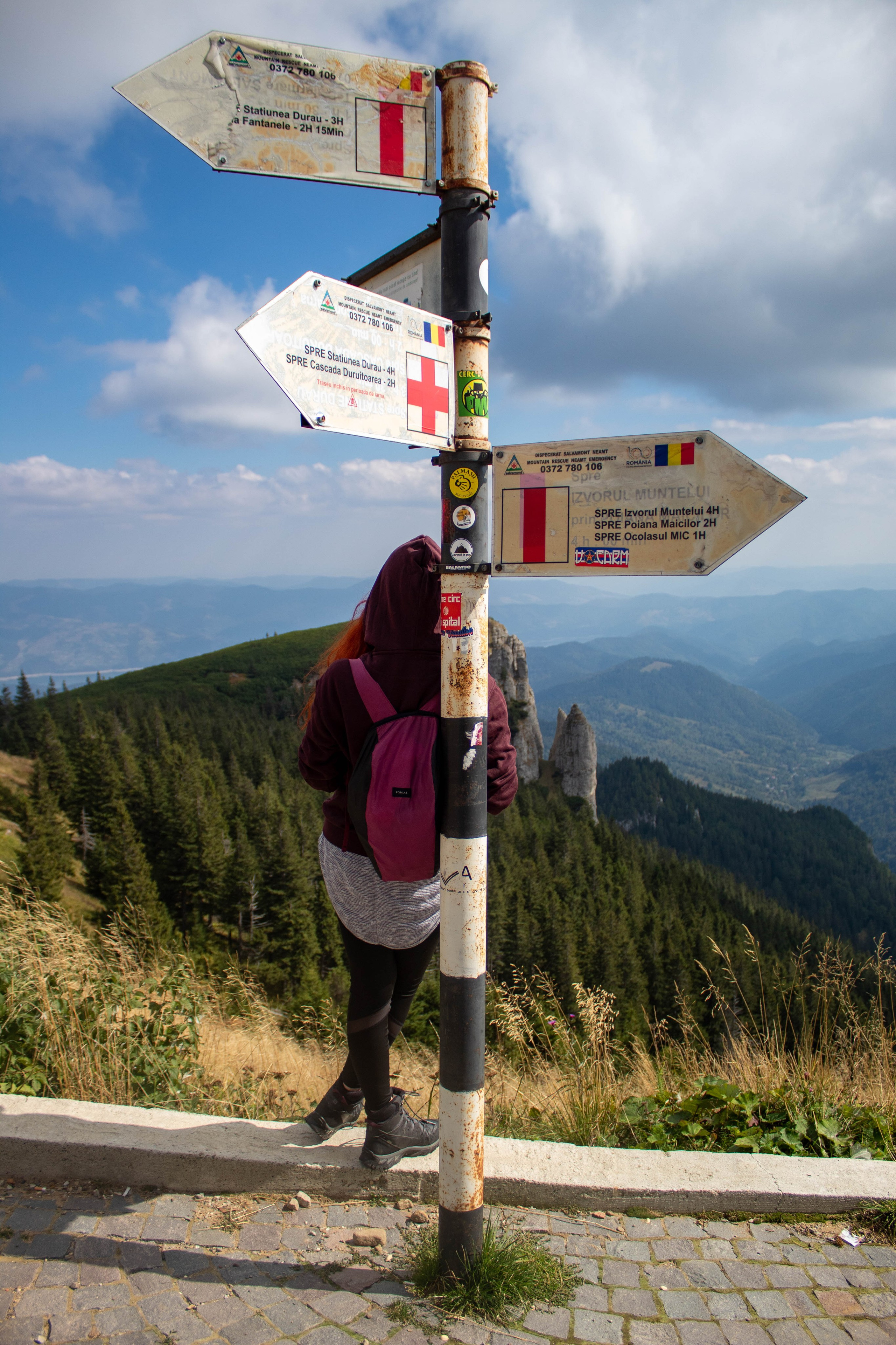 Hiker stretching next to trail signposts under the bright sun with mountain views.