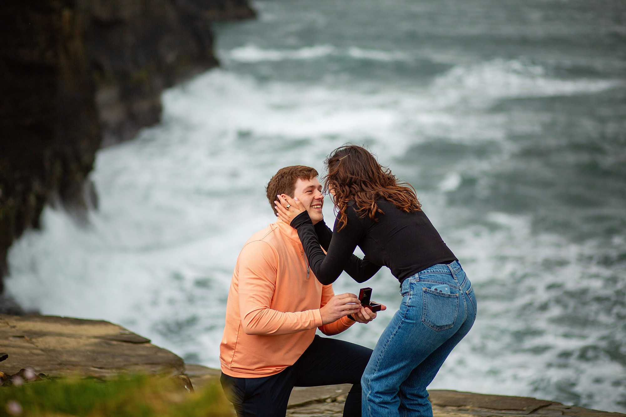 A close-up of a newly engaged couple celebrating their marriage proposal on the cliffs of Ireland.