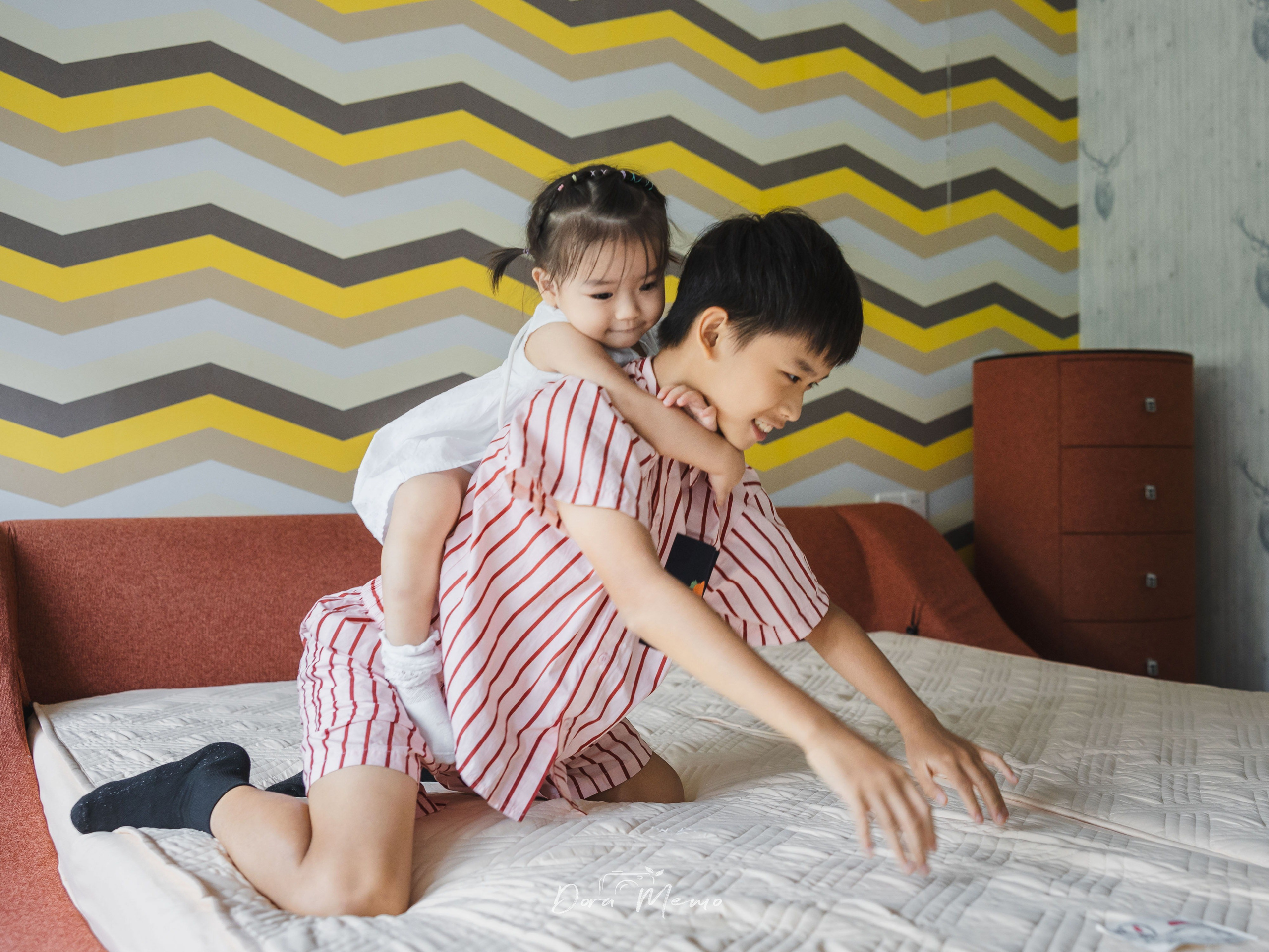 Brother gives his little sister a playful piggyback ride on the bed during an at-home family session.