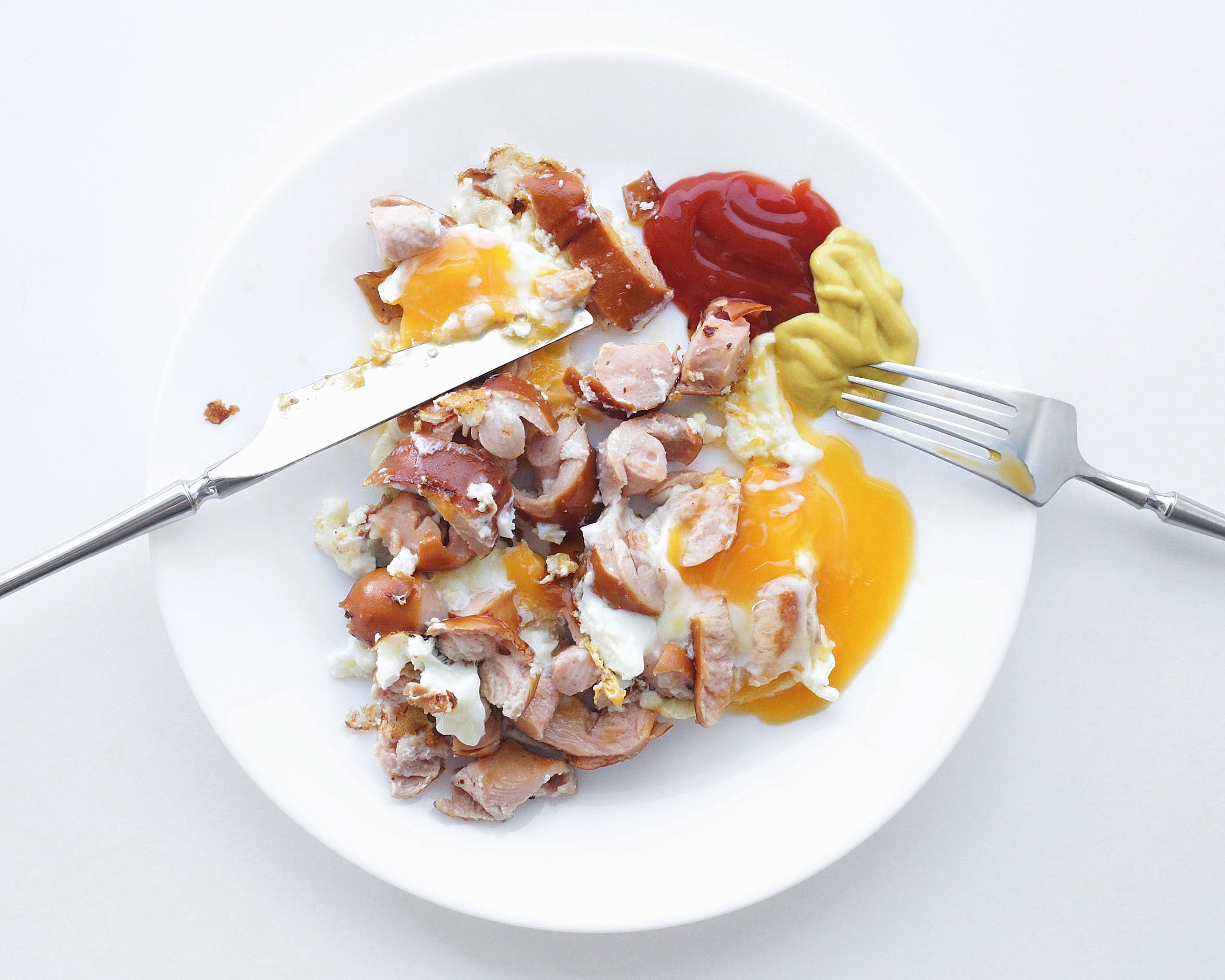 Minimalist breakfast plate with a fried egg and grilled sausages, garnished with ketchup and mustard on a white plate