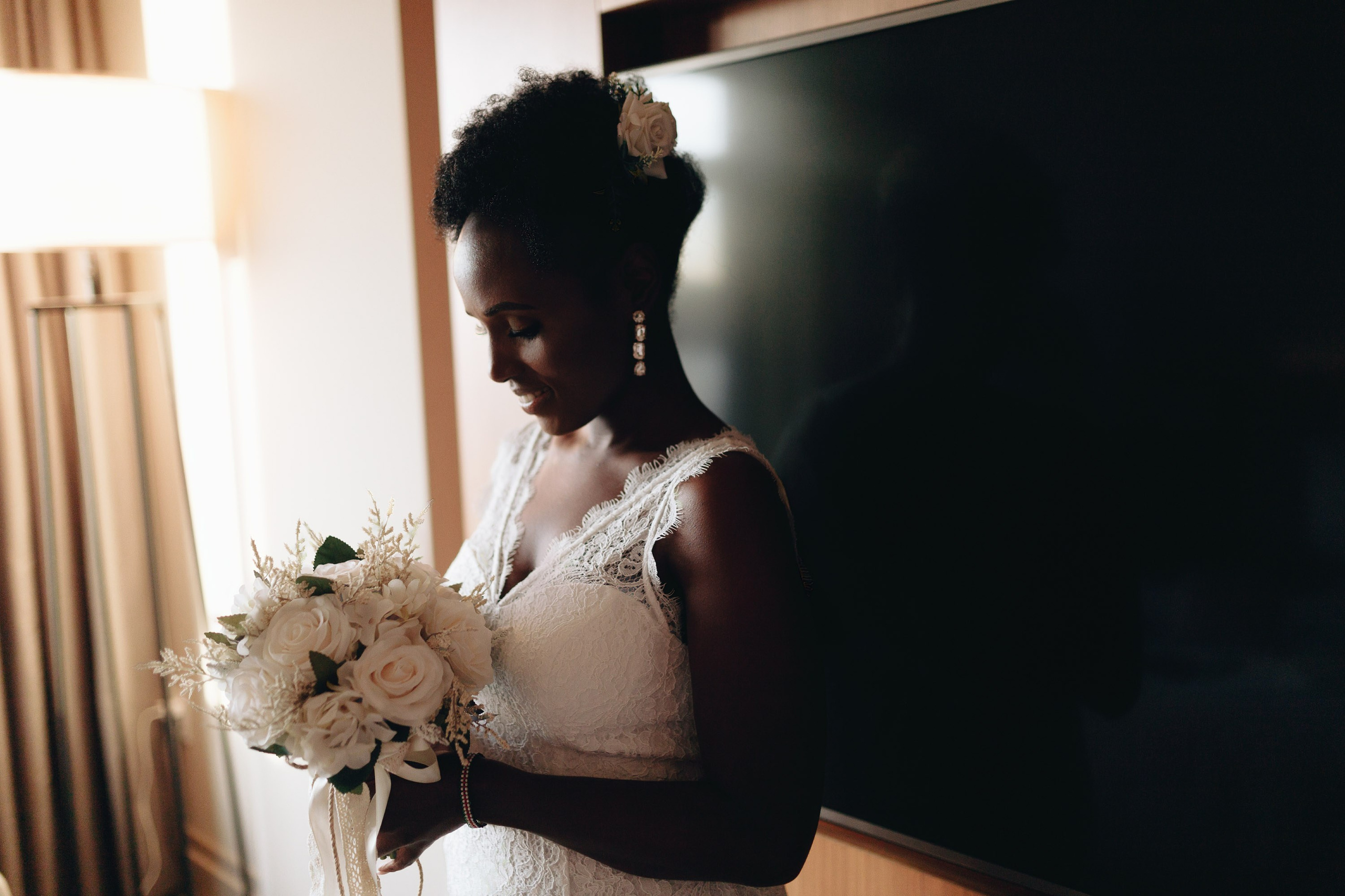 Bride looking at bouquet by window, intimate wedding moment