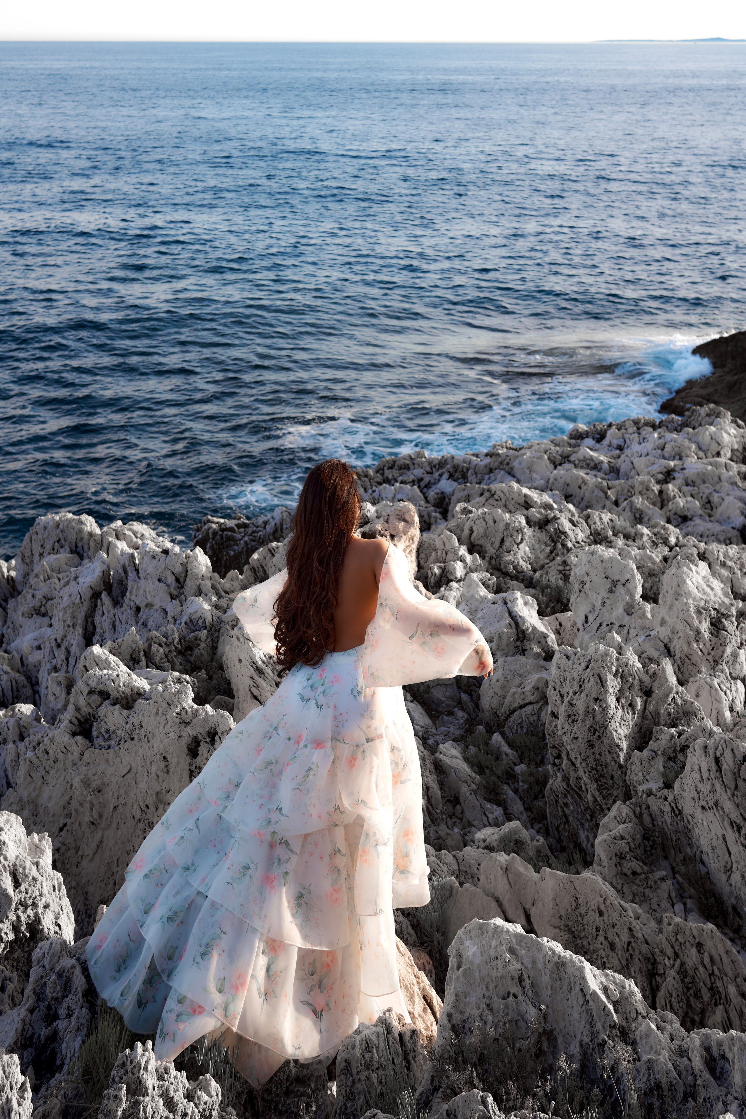 Fashion photo of woman with long hair in sheer blue dress on rocky coastline Saint-Jean-Cap-Ferrat