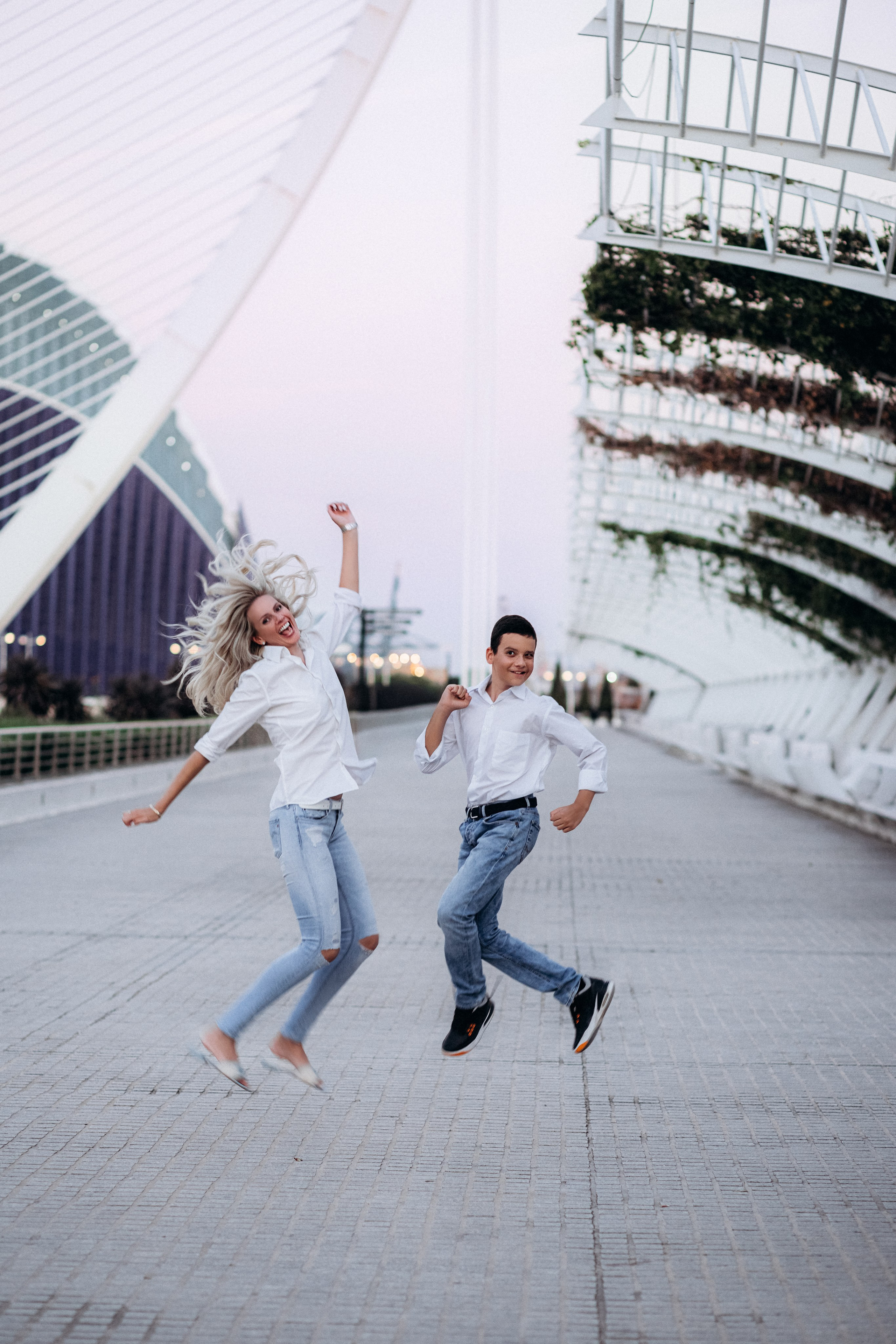 Alegre sesión de fotos familiar en Valencia, España, capturando a una madre y su hijo saltando de emoción frente a la Ciudad de las Artes y las Ciencias — ideal para quienes buscan sesiones familiares vibrantes y enérgicas en Valencia y España.