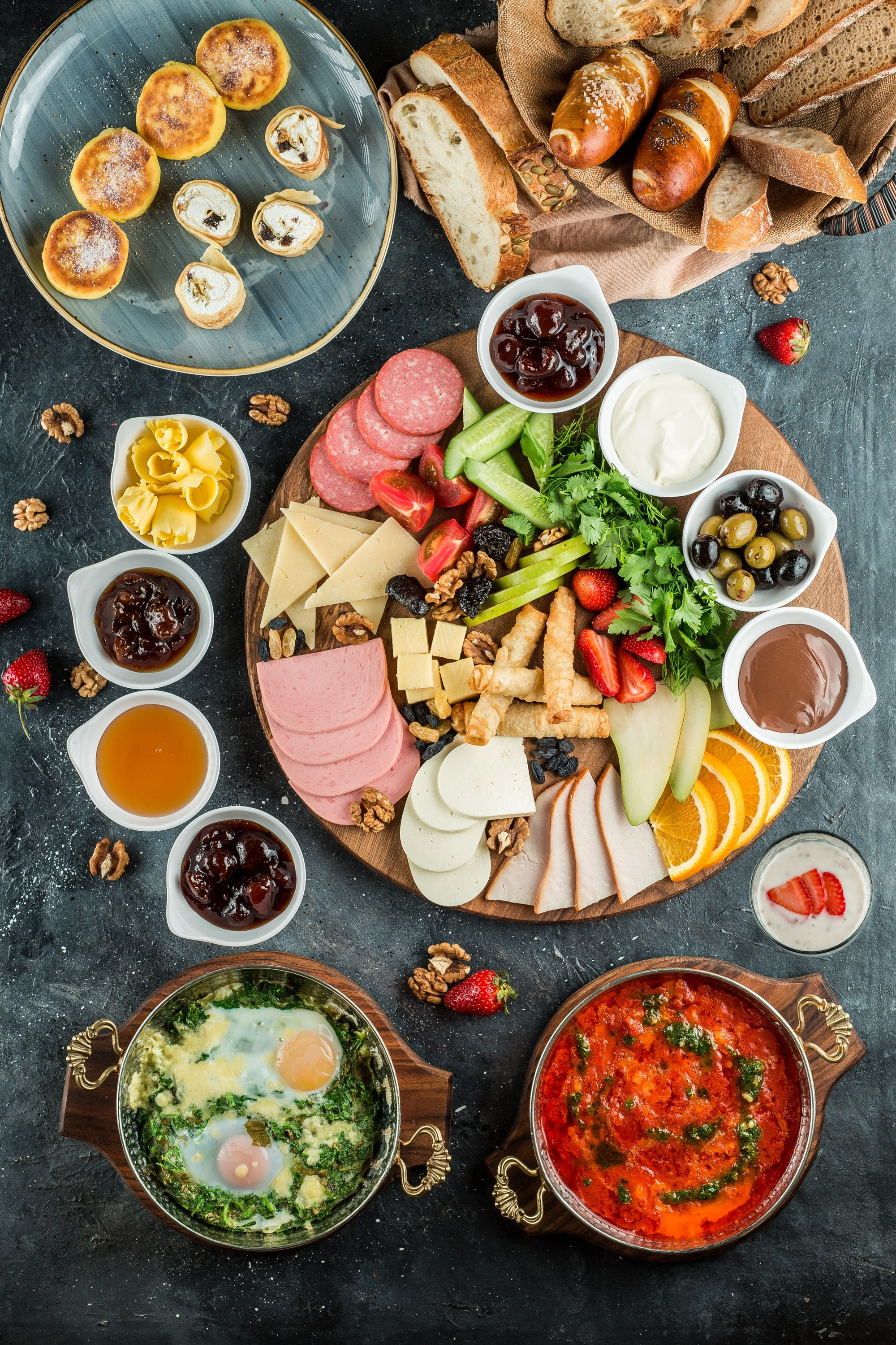 Səhər yeməyi üçün pendir, kolbasa, təzə tərəvəz, zeytun və souslarla zəngin plater, yanında qayğanaq və pomidor sousunda yumurta.