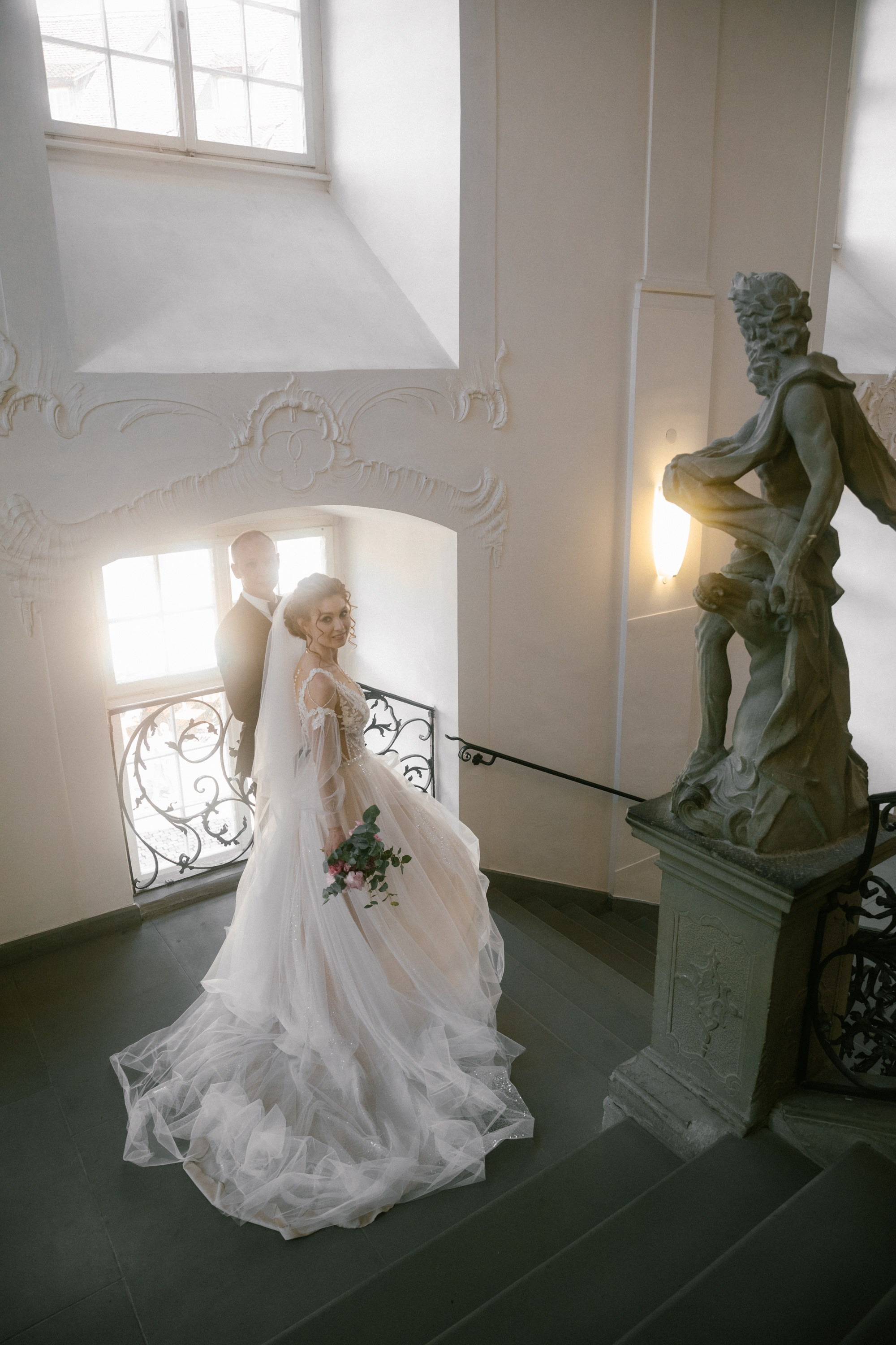 Bride and groom walking down castle staircase with sunlight streaming through window