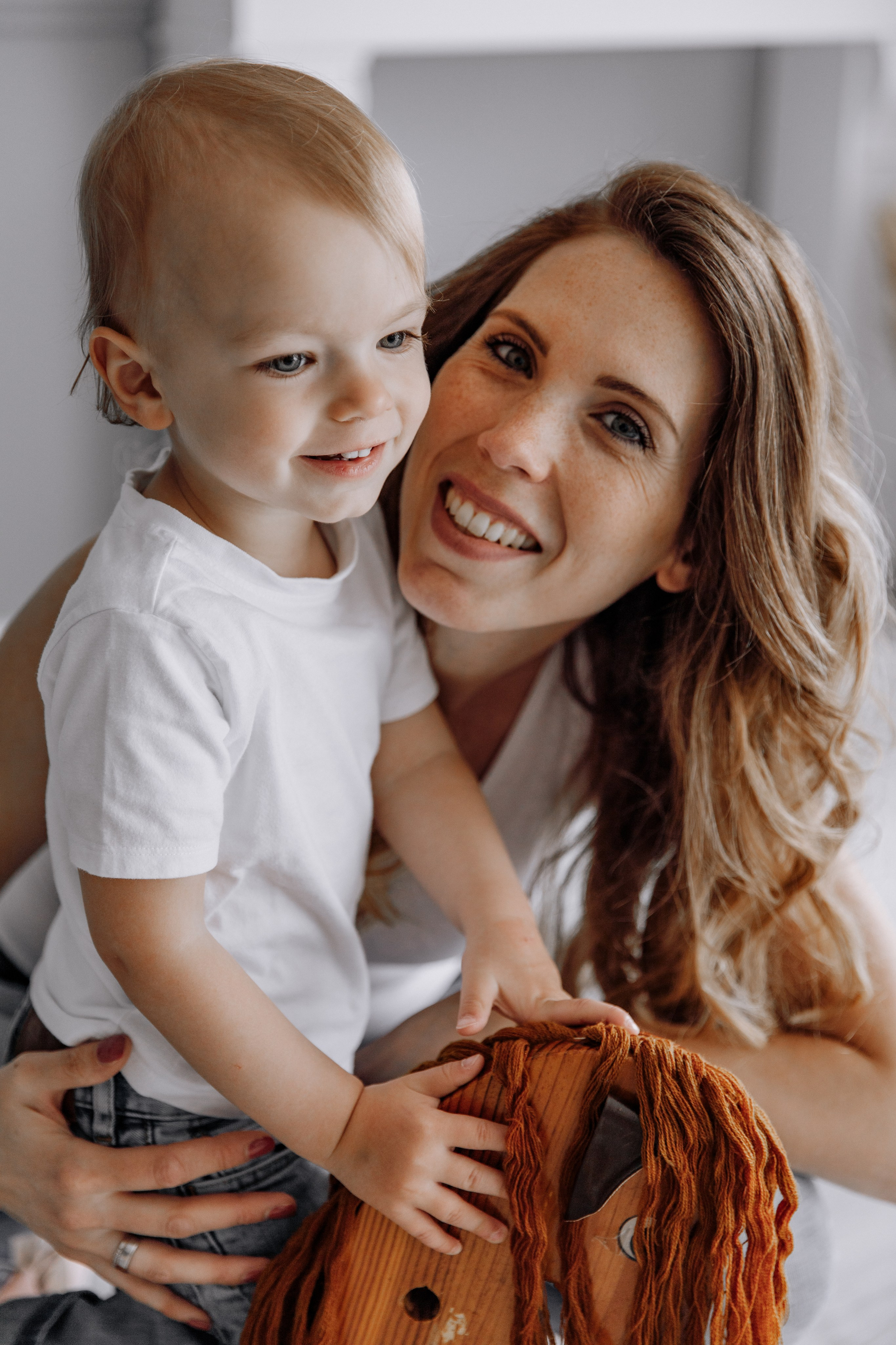 Mutter und Sohn lächeln, während der Sohn auf einem hölzernen Schaukelpferd reitet.