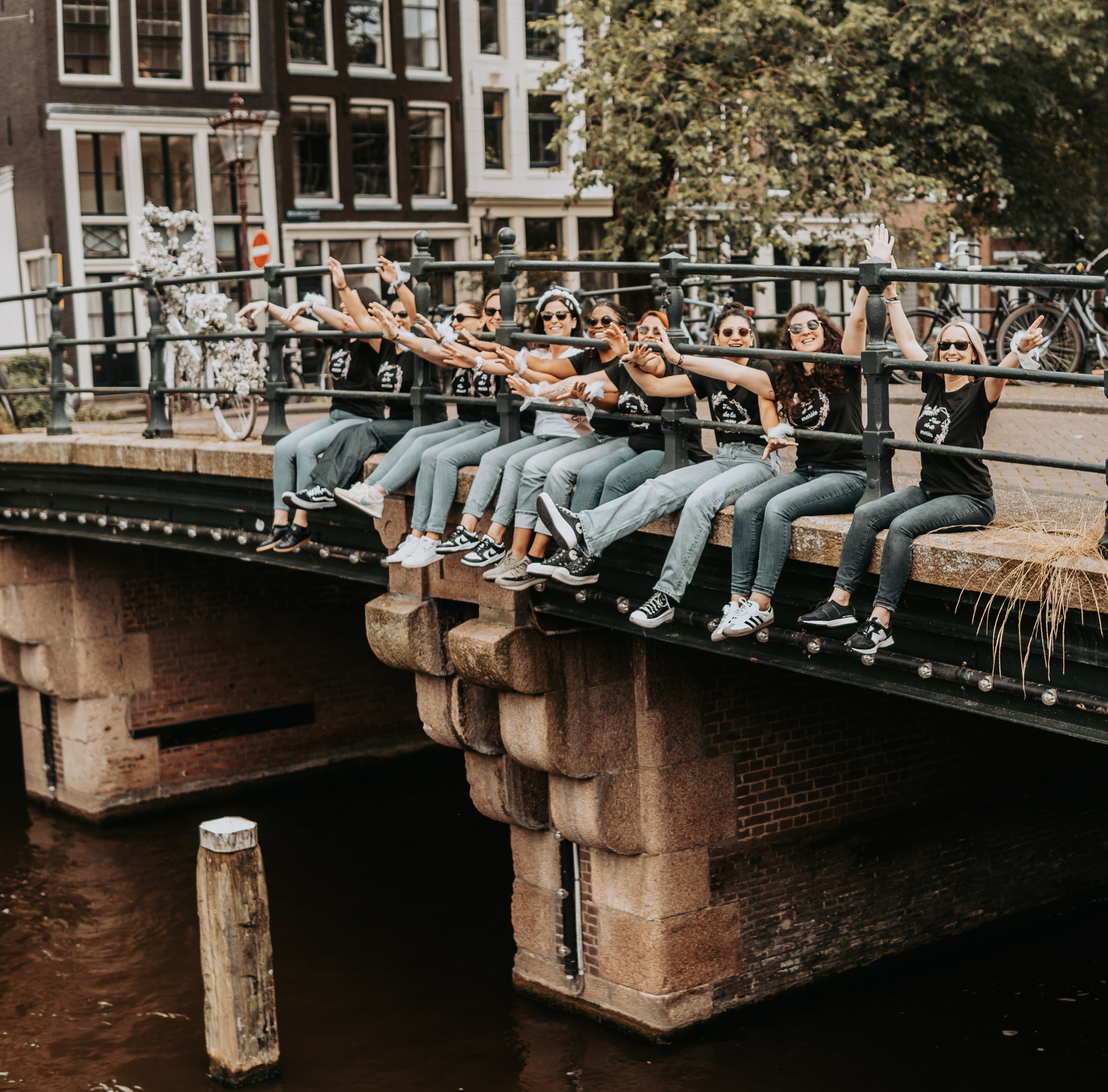 girls and bride to be sitting on ground near a canal in amsterdam