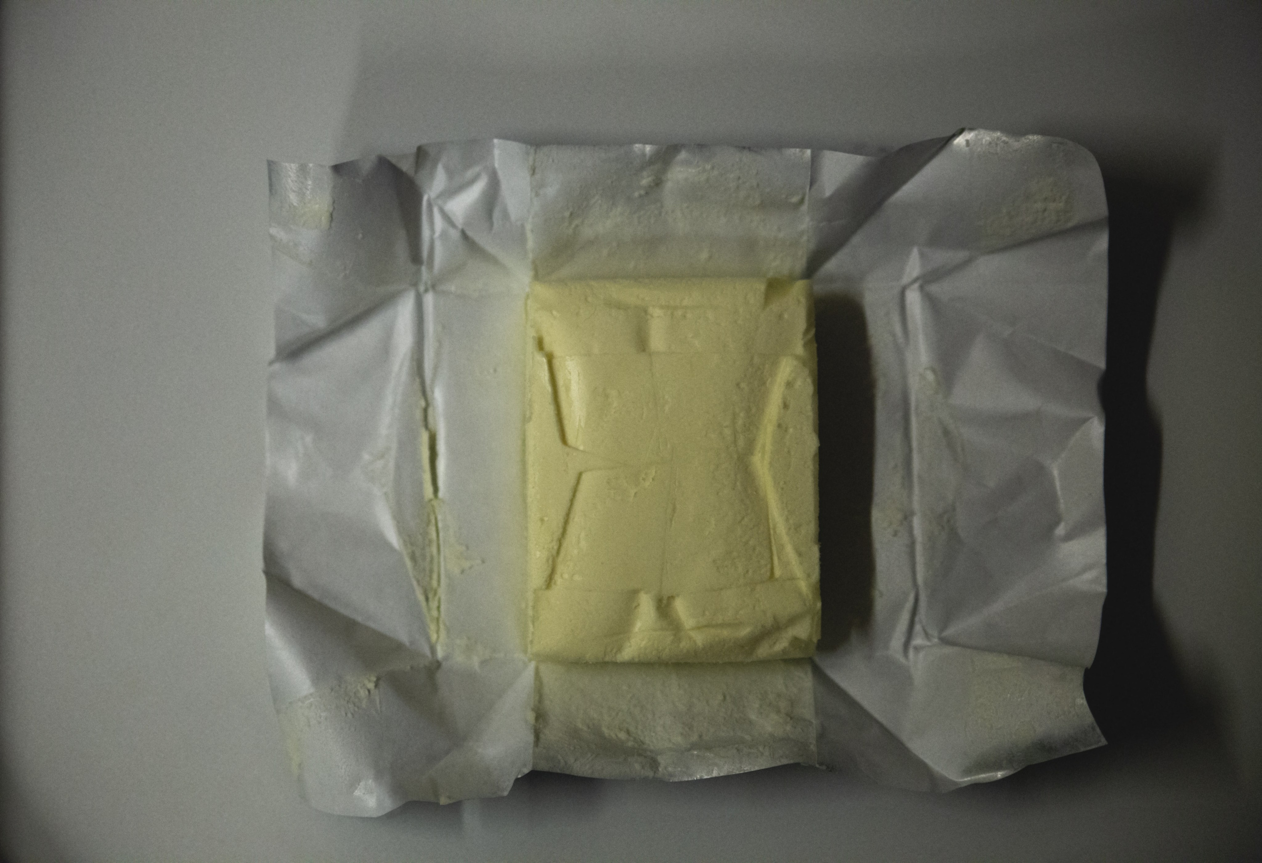 Unwrapped block of butter resting on its crinkled paper wrapper, shot in soft light to emphasize everyday simplicity and texture in food styling