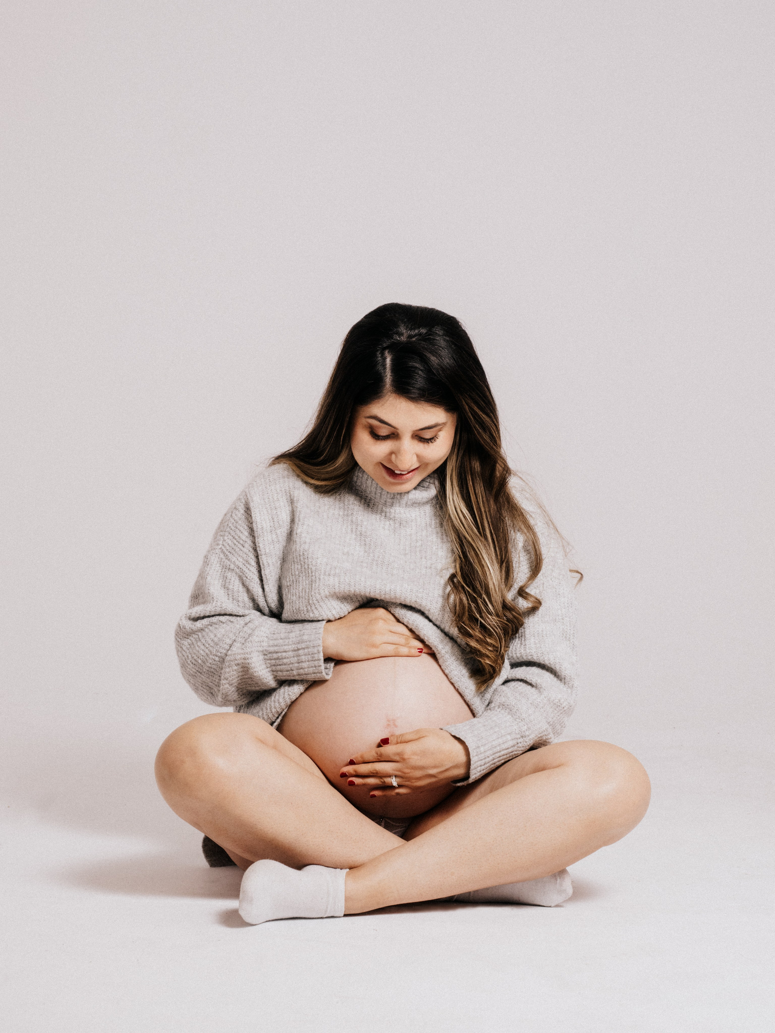 Pregnant woman sitting cross-legged in a photo studio.