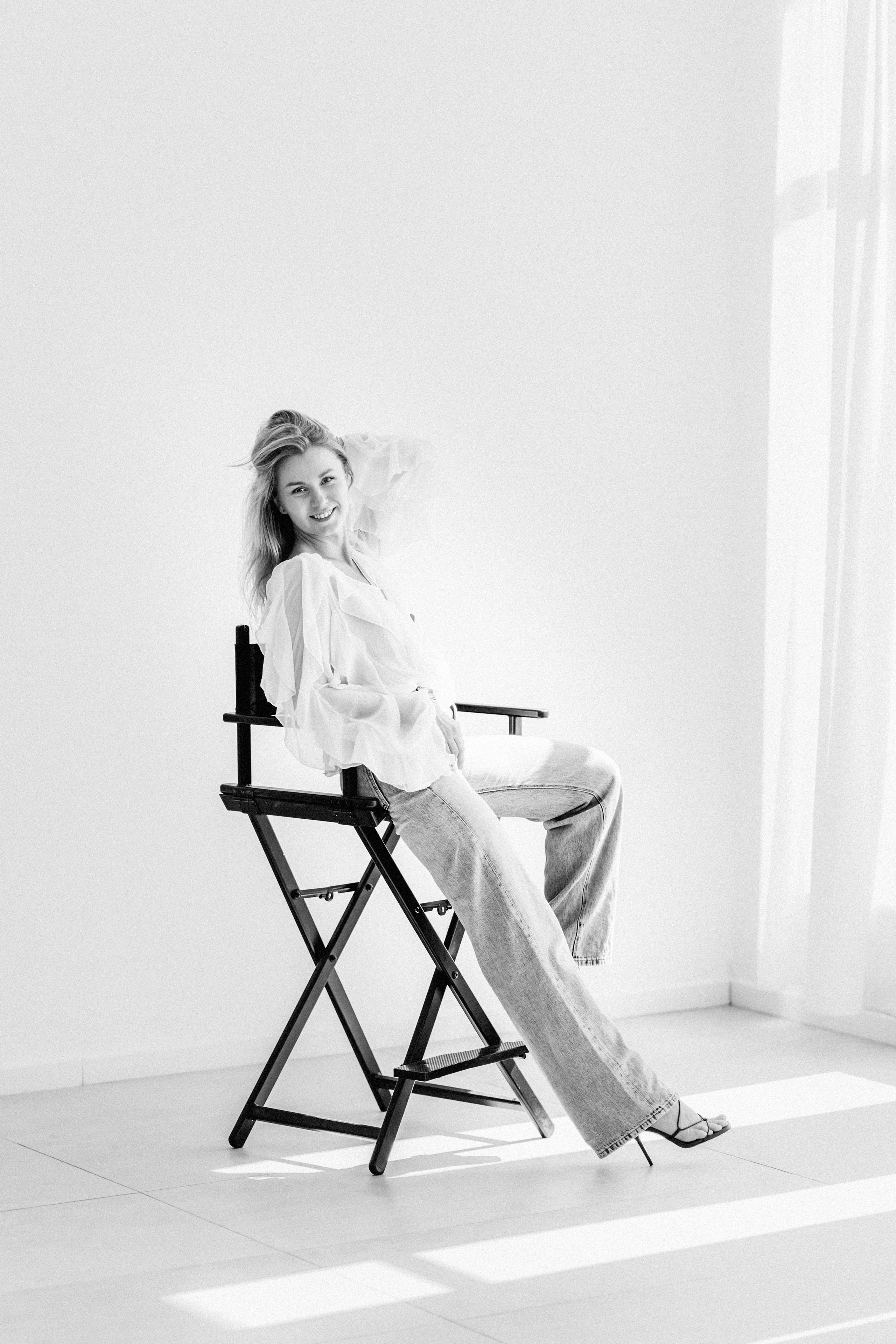 Черно-белый женский портрет, снятый в Валенсии, Испания, с расслабленной и уверенной женщиной, сидящей на режиссерском кресле в минималистичной студии — идеально для персонального брендинга и редакционных фотосессий в Валенсии и по всей Испании.