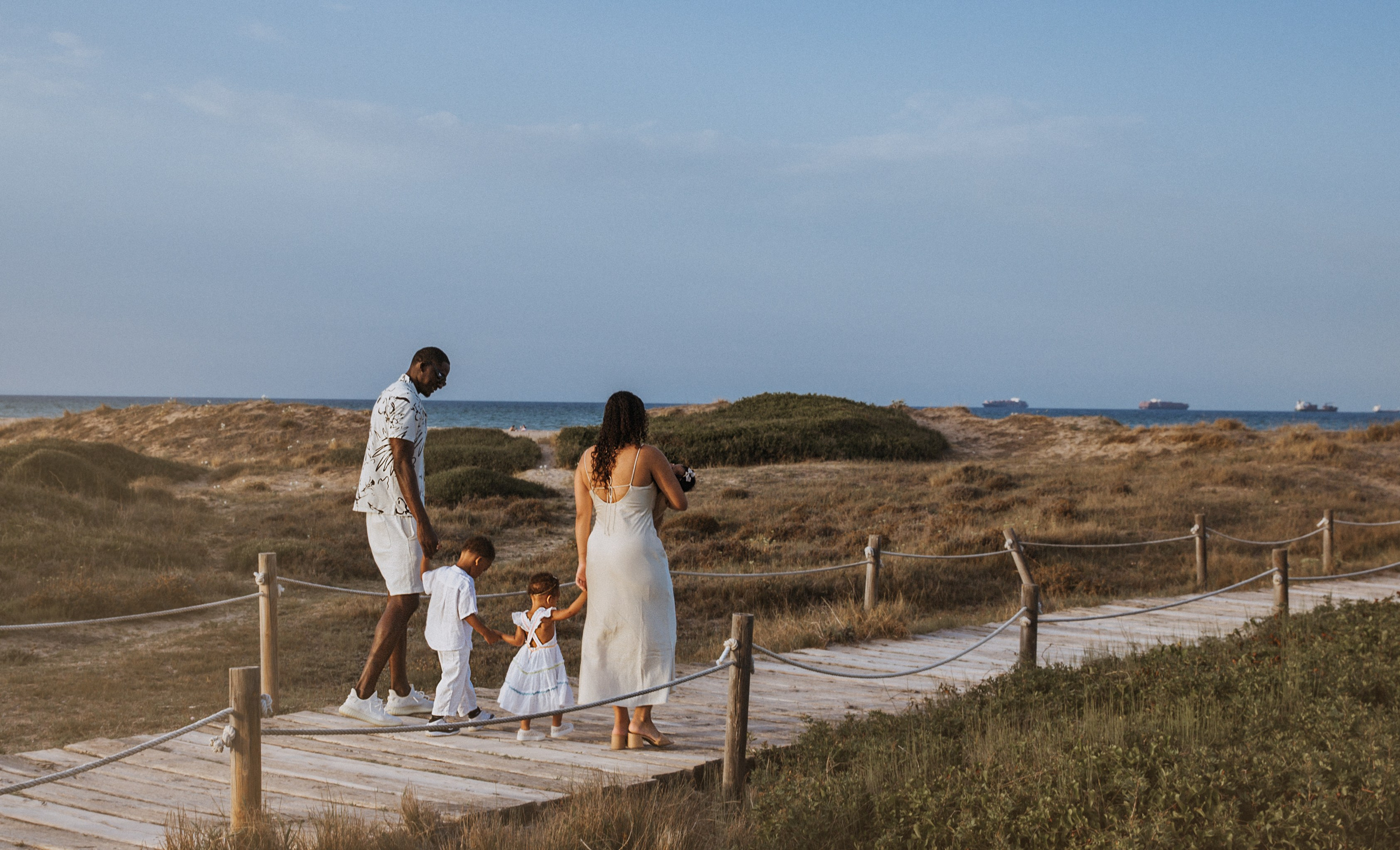 Familia caminando de la mano por un sendero escénico de playa al atardecer en Valencia, España — capturando un momento espontáneo y entrañable, ideal para sesiones familiares naturales.