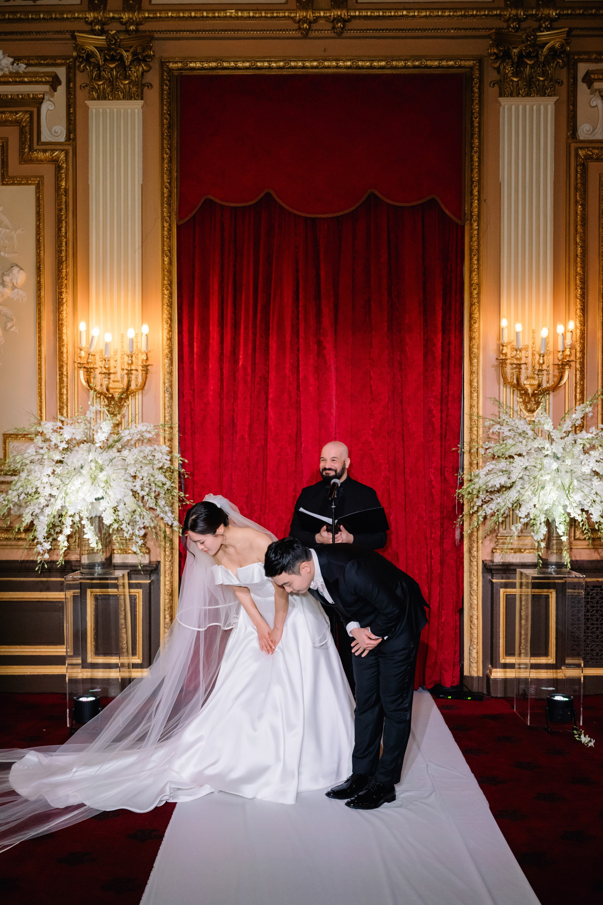 a bride and groom kissing in front of a red curtain