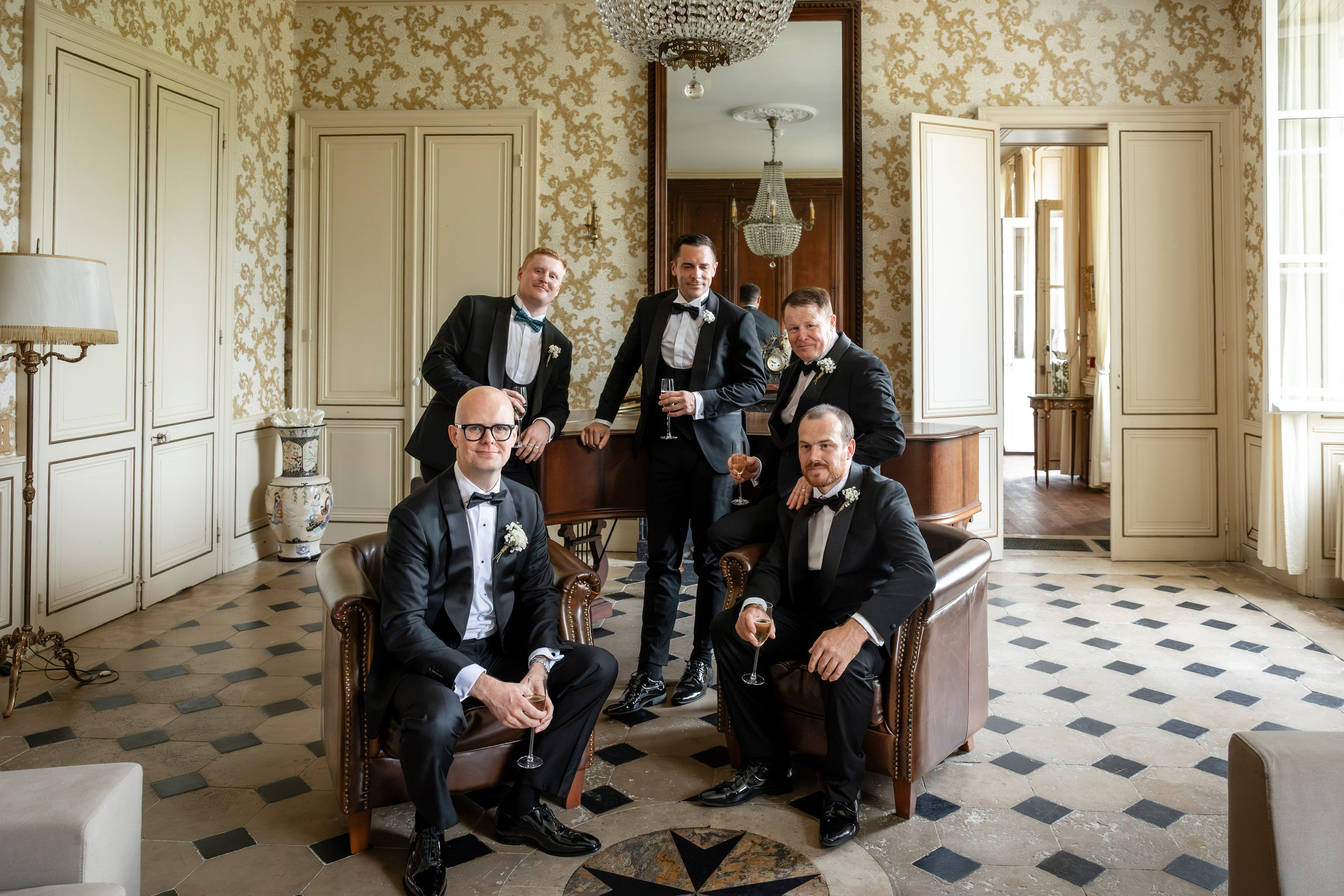 Groom and groomsmen in black tie in the chequered-floor hall of the château