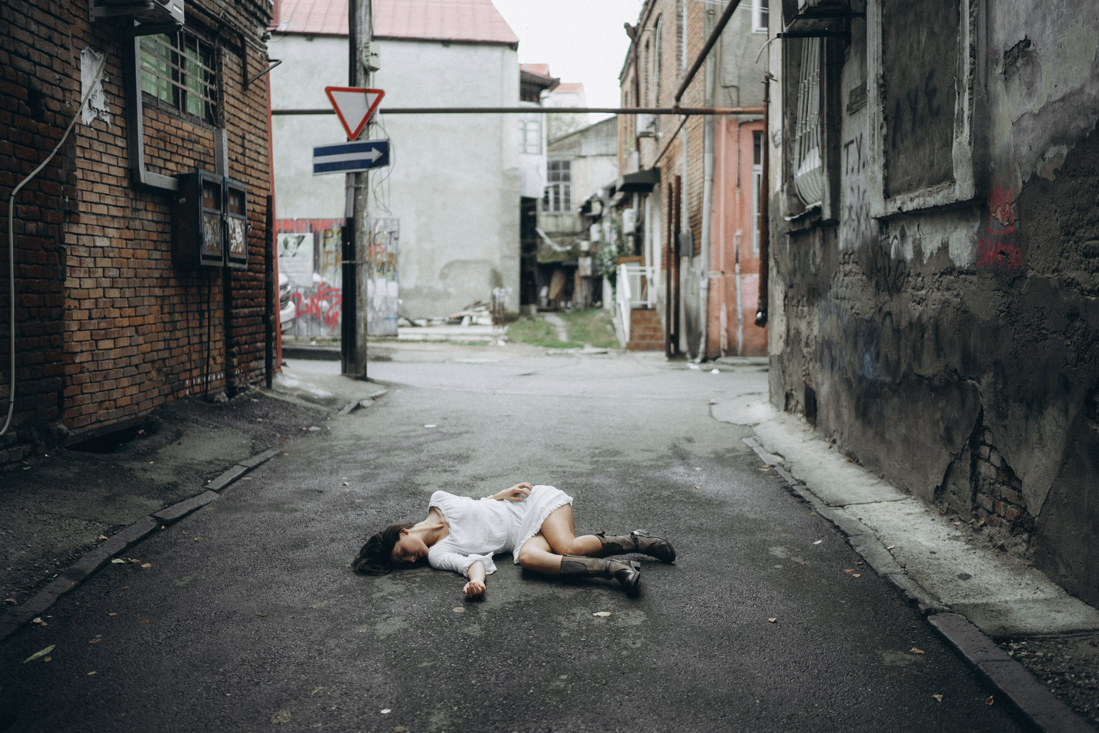 Frau in weißem Kleid liegt auf dem Boden einer Gasse – künstlerische Portraitfotografie Dresden