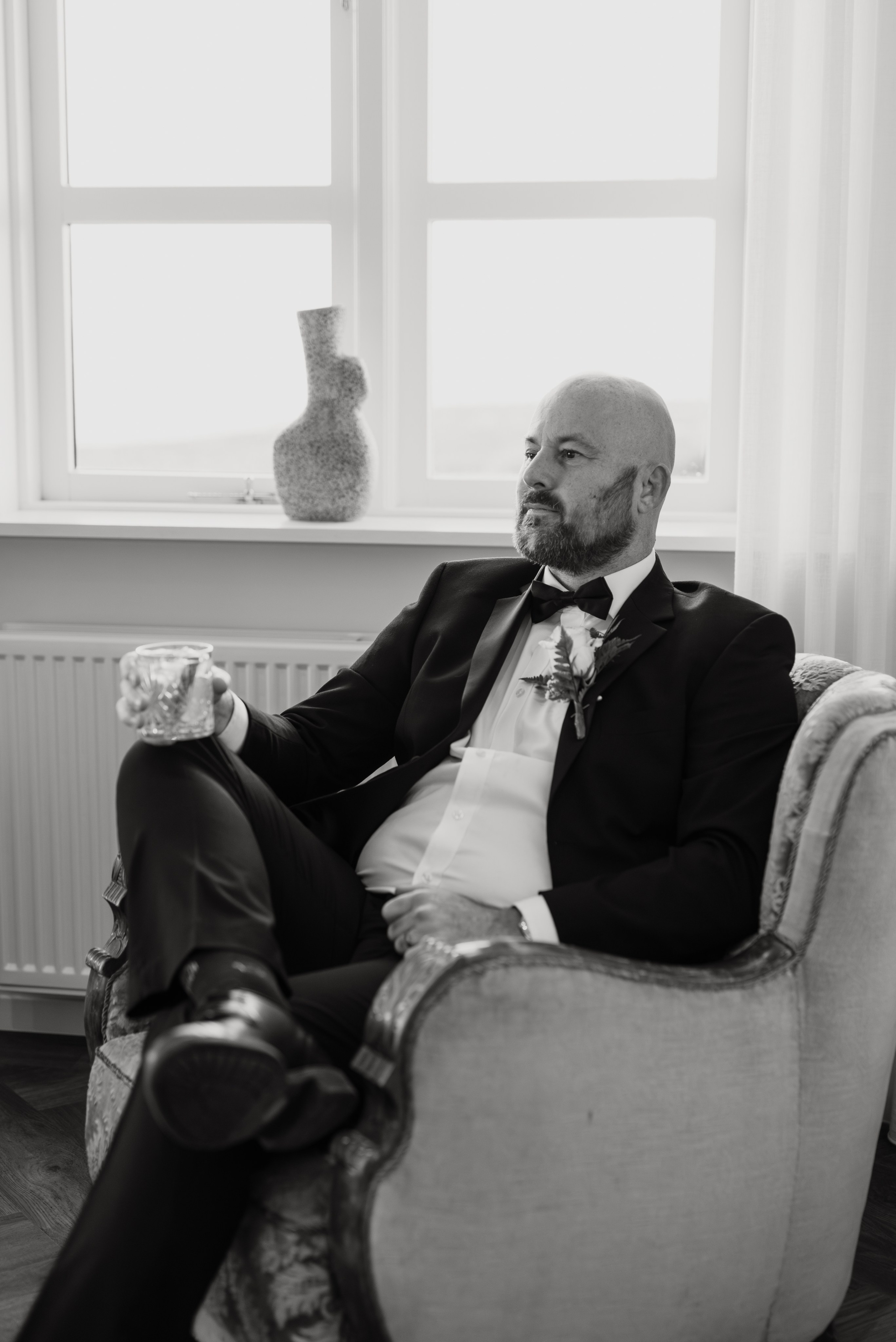 Intimate embrace between the bride and groom near the black church of Búðir, framed by rolling hills and an overcast sky.