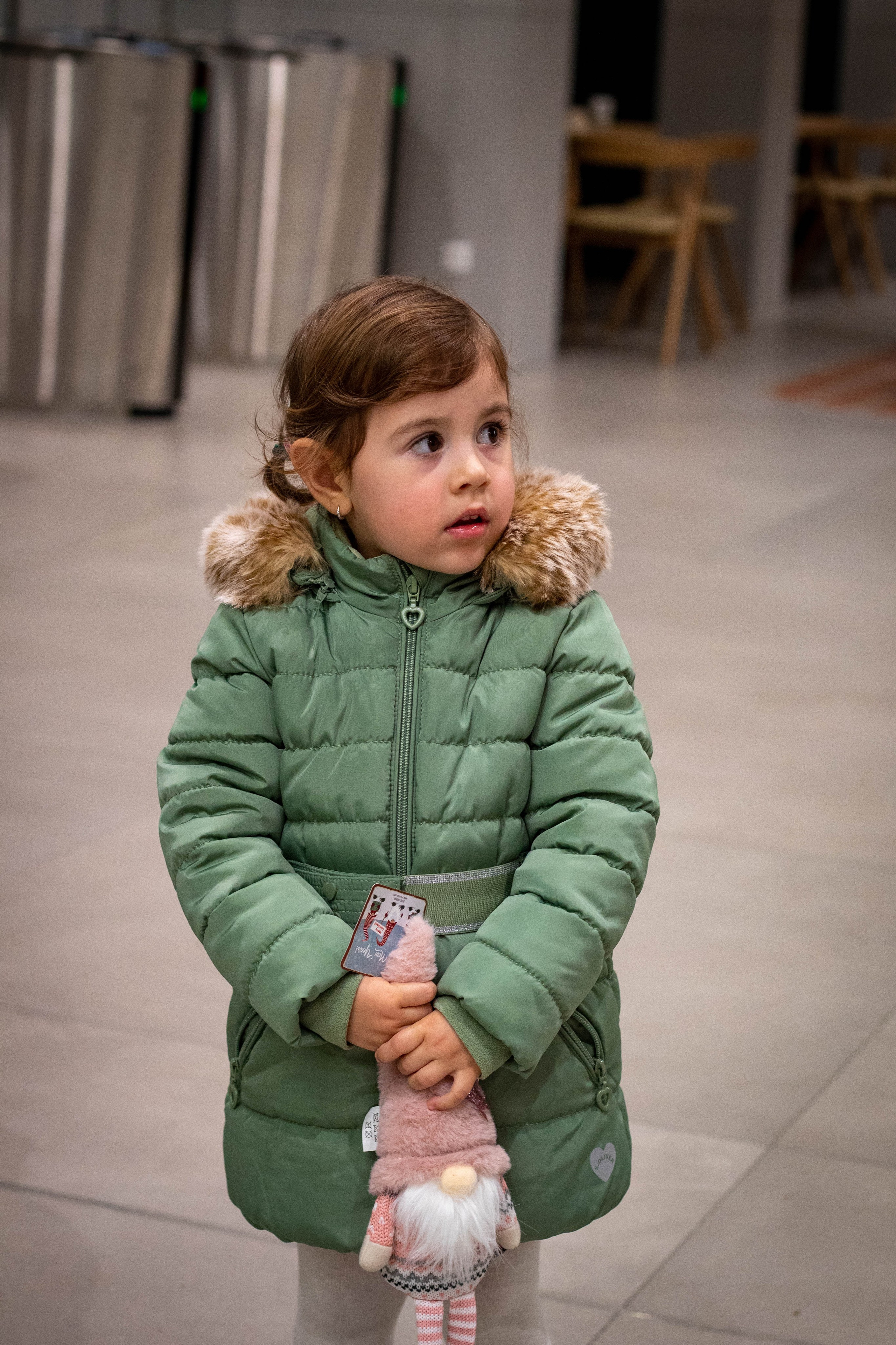 Toddler standing alone in a green outfit, learning to balance indoors.