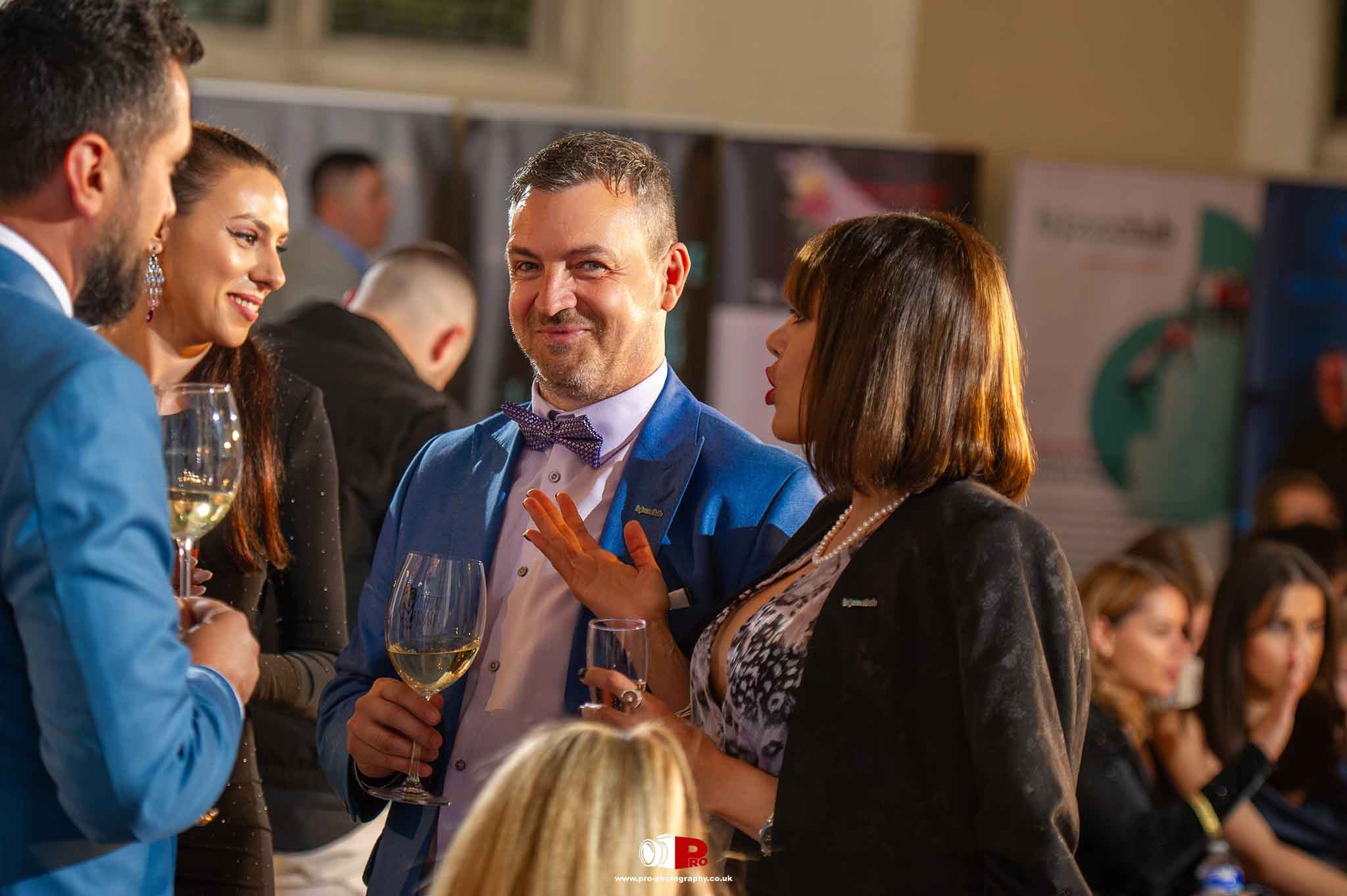 A group of elegantly dressed attendees converse with wine glasses at a high-end networking event.