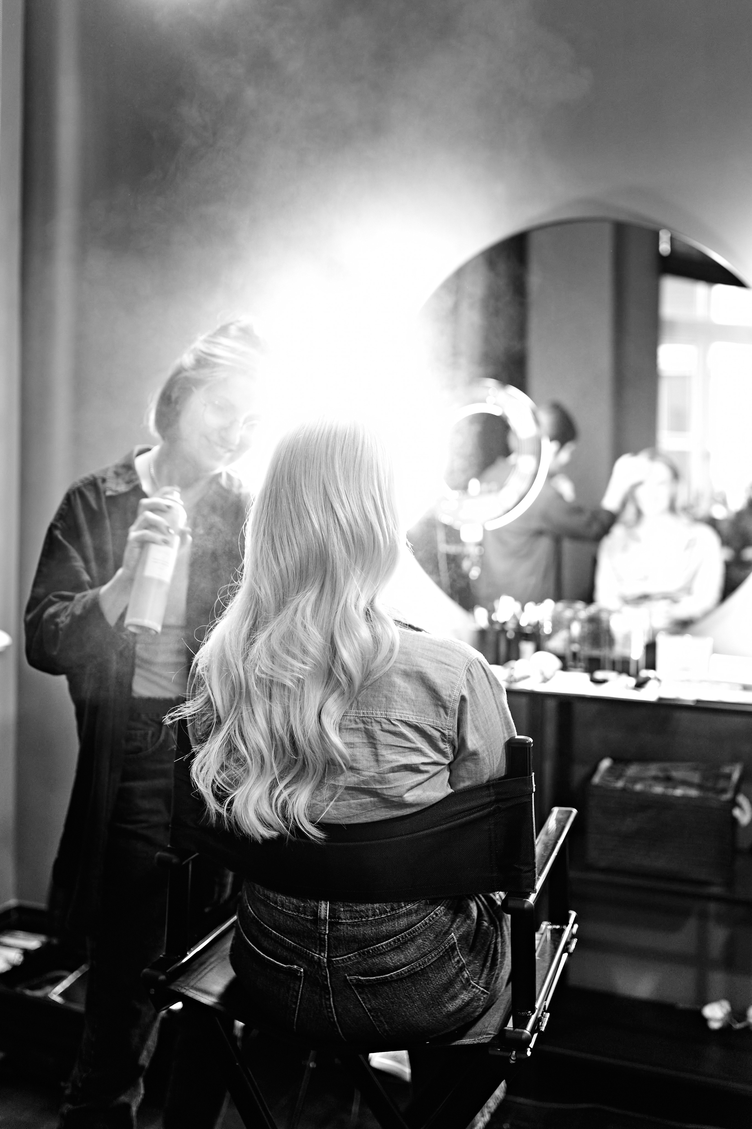  A behind-the-scenes photo of a stylist working on a client’s hair in a brightly lit studio space.