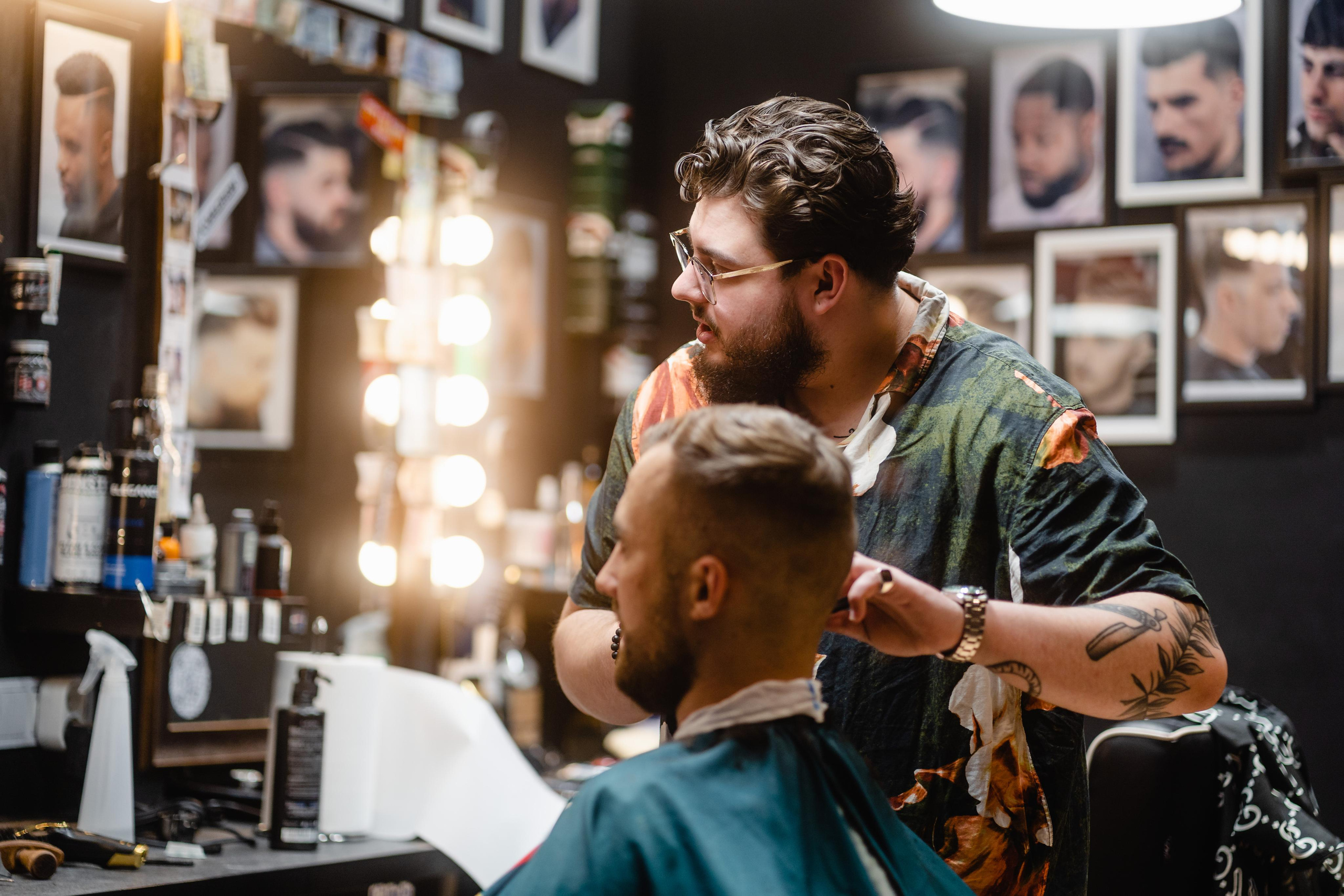 A barber carefully trimming a client’s hair in a vibrant barbershop filled with warm lighting and mirrors.