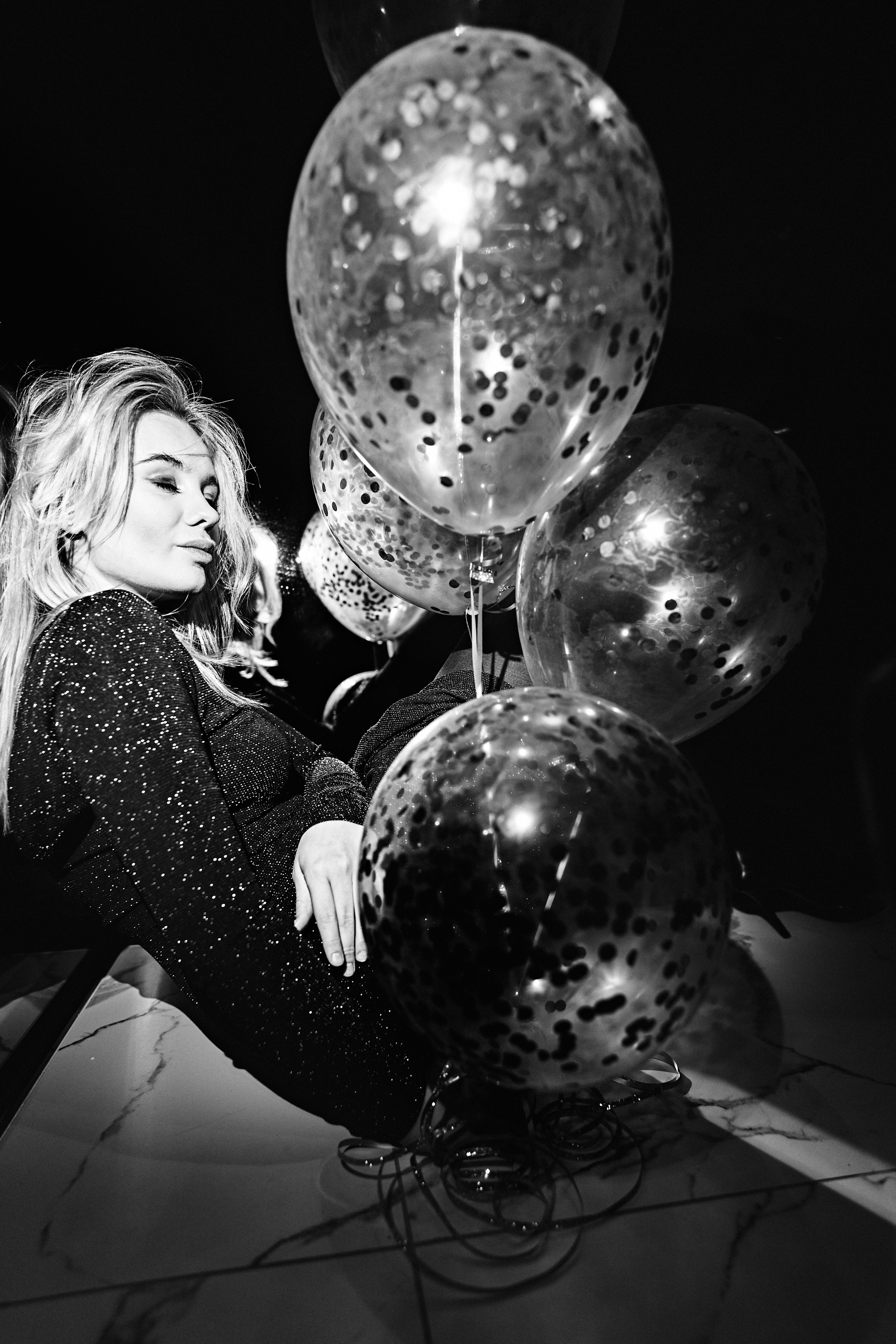 A woman holding reflective balloons while wearing an elegant outfit, set against a luxurious backdrop.