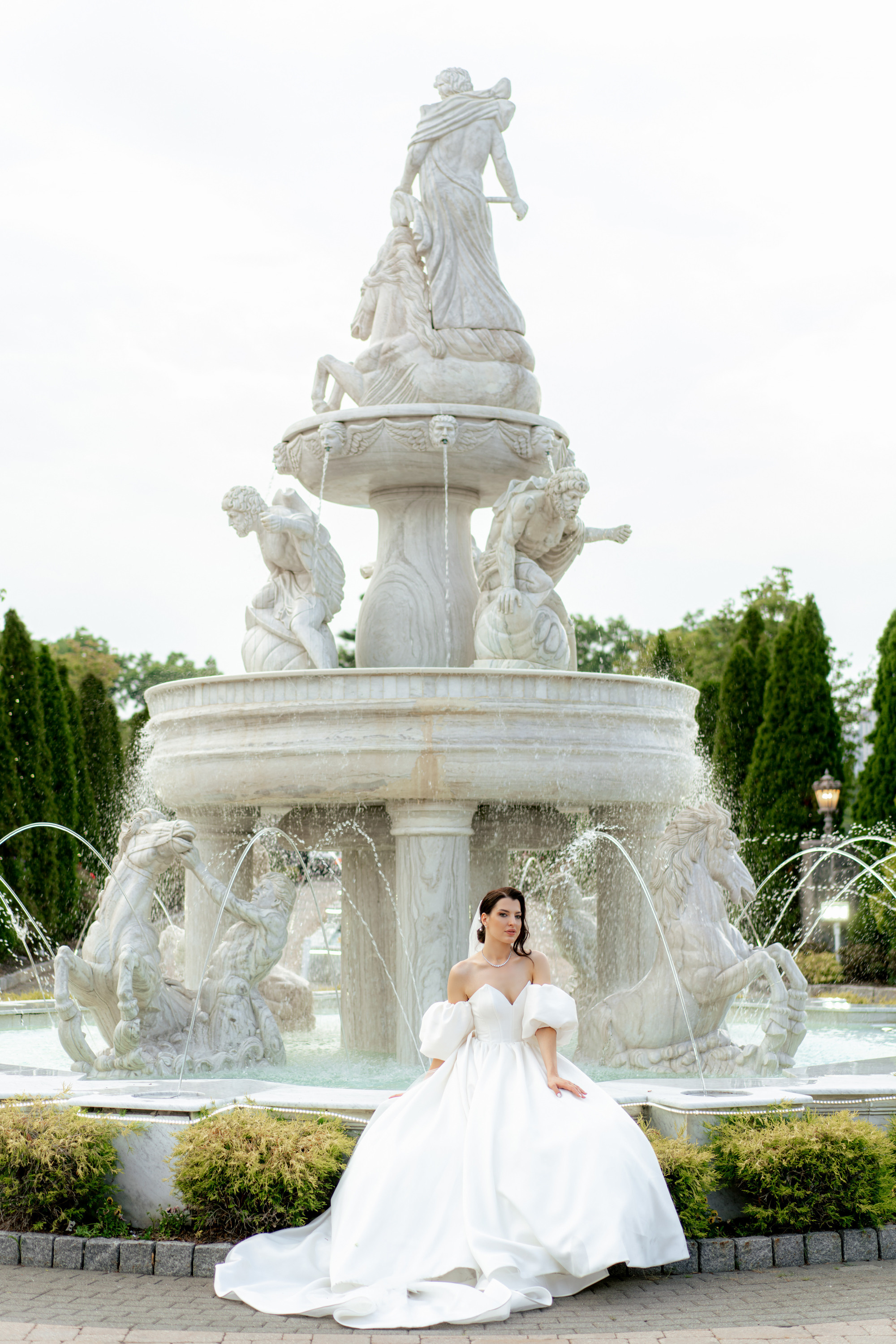 a bride sitting on a fountain in front of a fountain