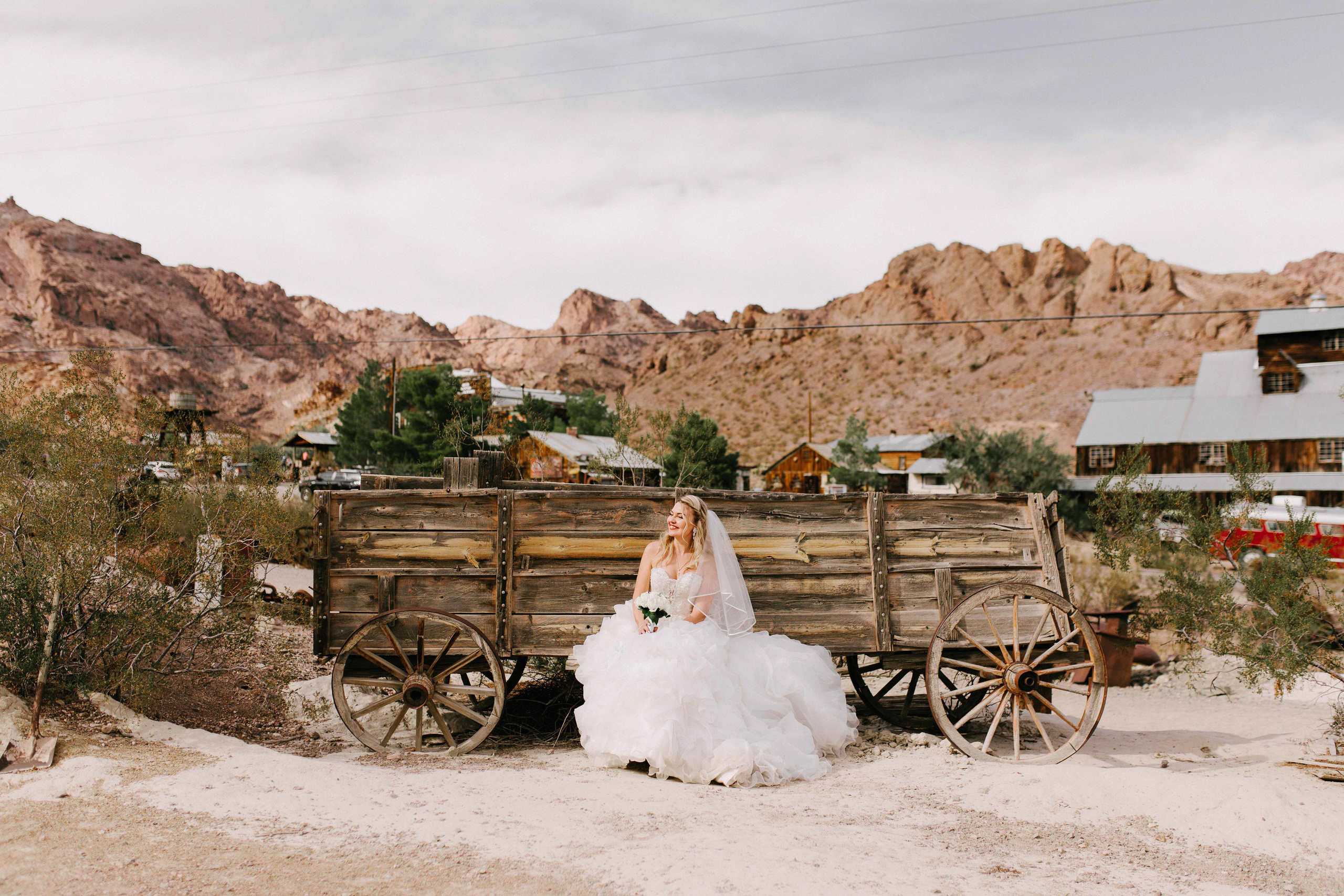 a bride in a white dress is sitting in front of a wagon