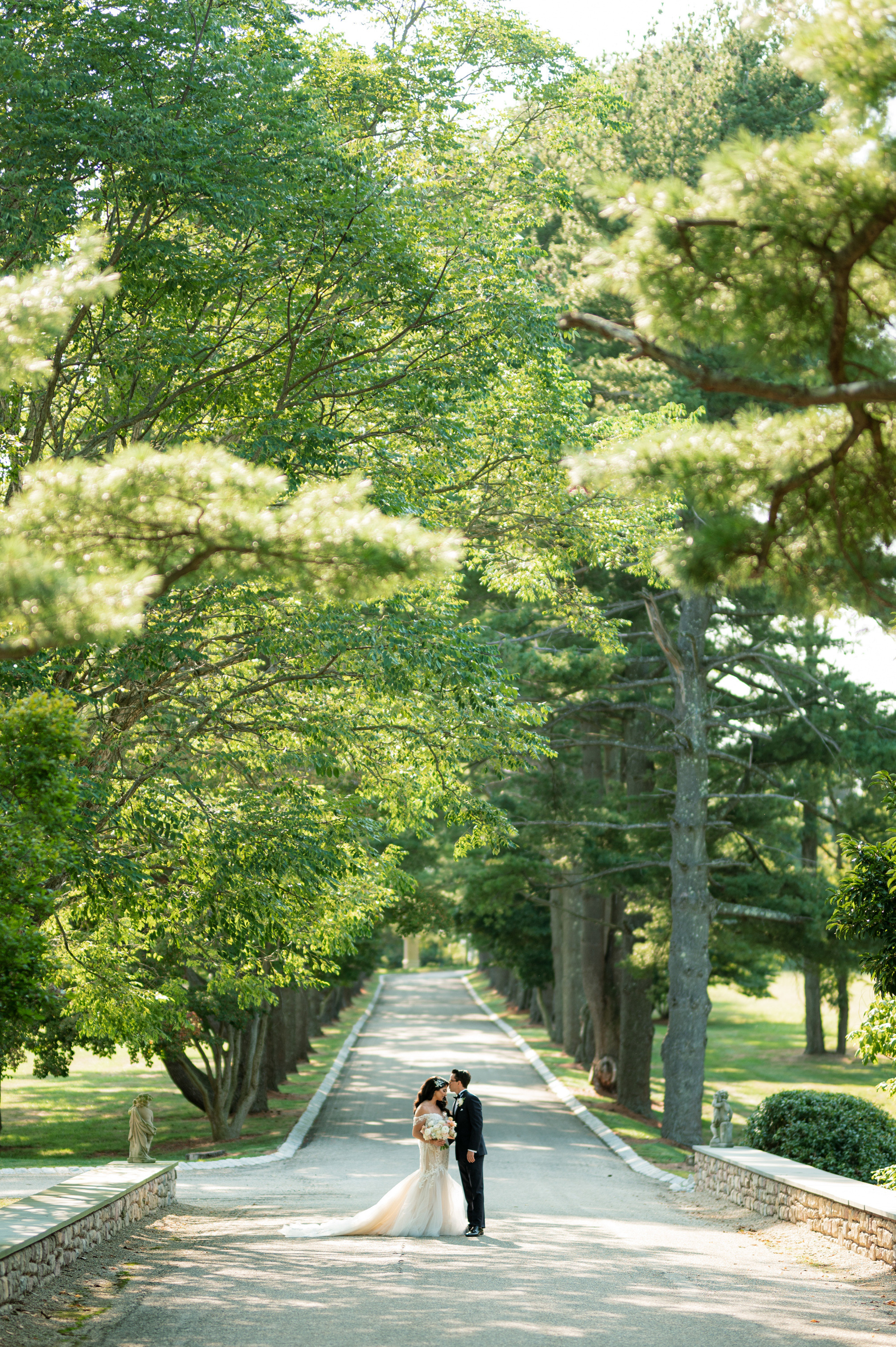 a bride and groom walking down the road in front of a tree