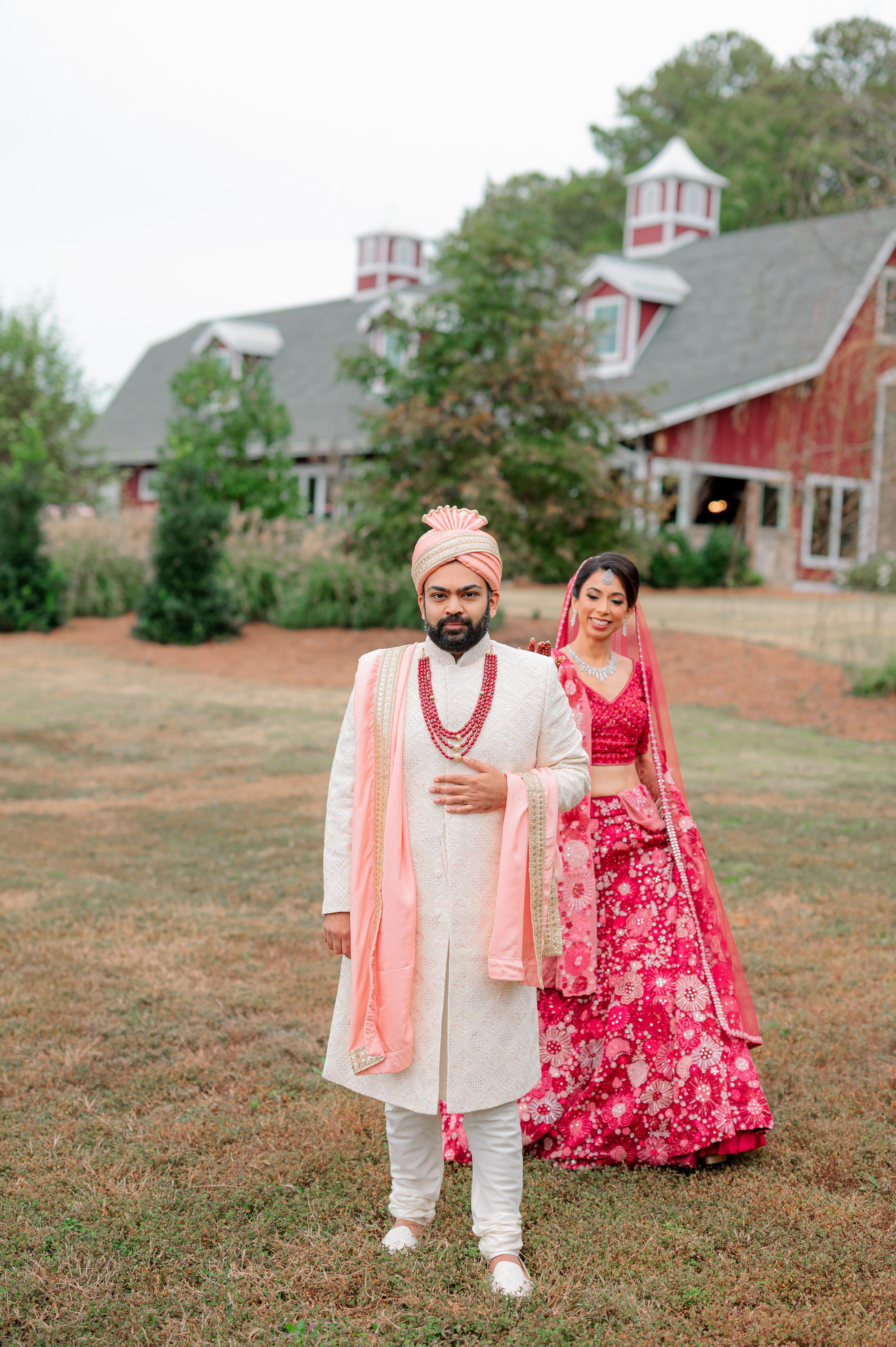 a bride and groom pose for a photo in front of a red barn