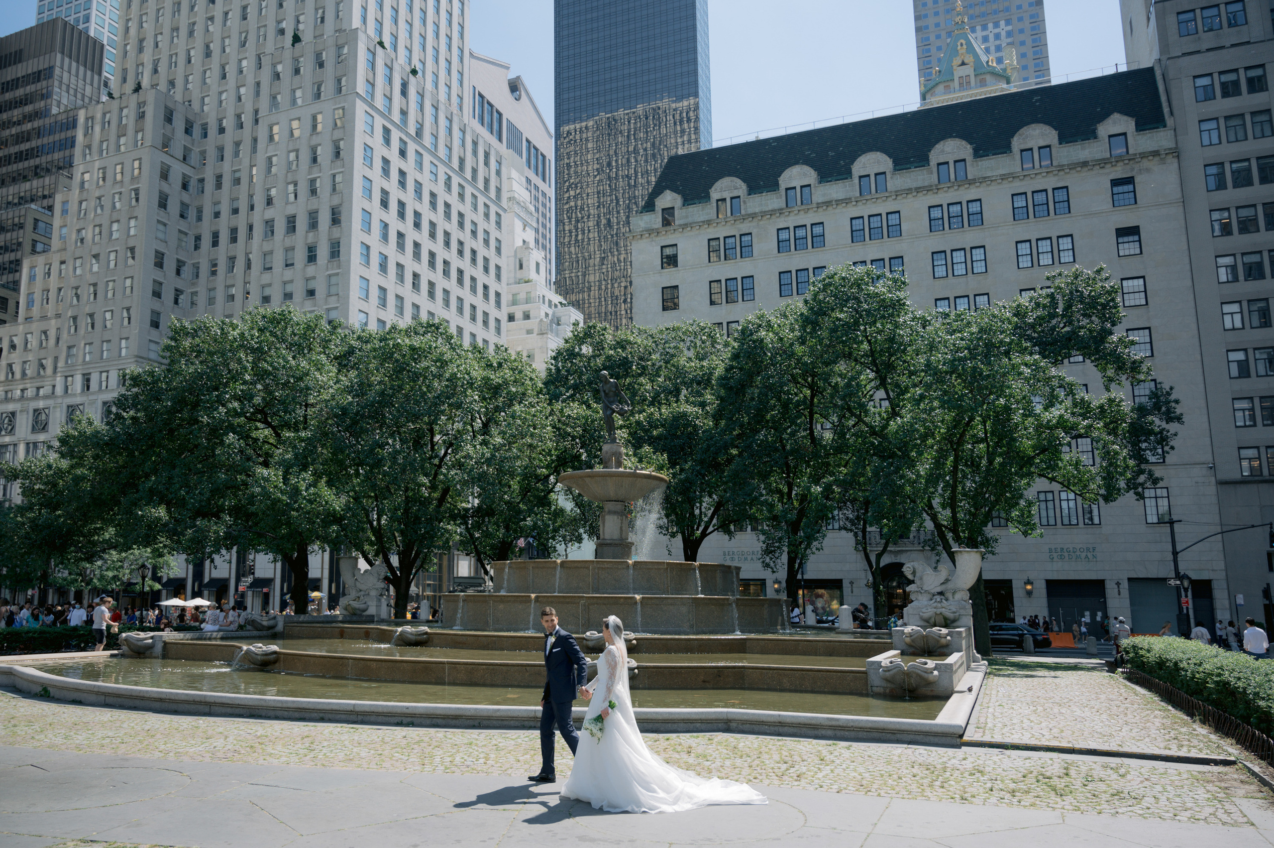 a bride and groom pose in front of a fountain