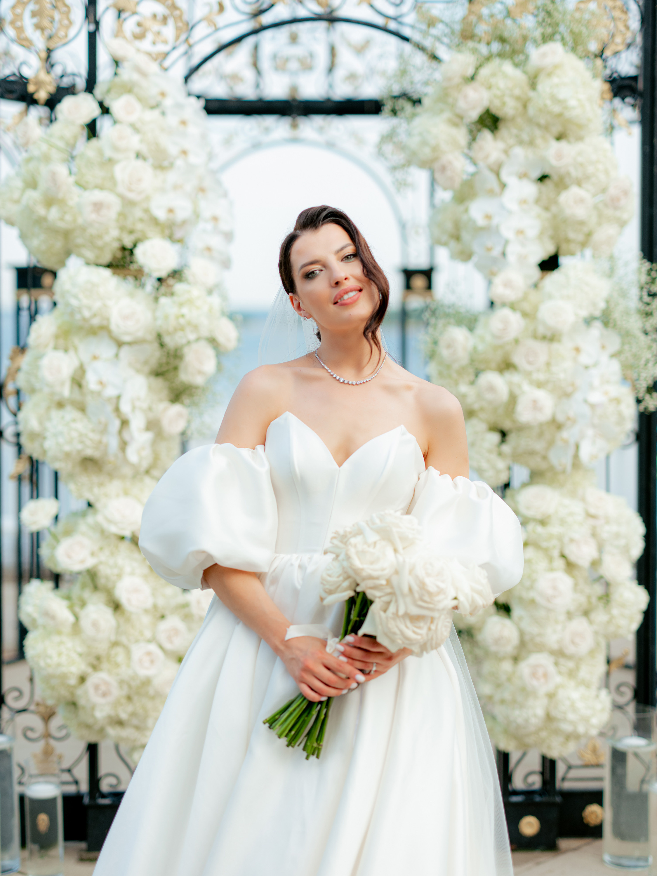 a bride in a white wedding dress standing in front of a floral arch