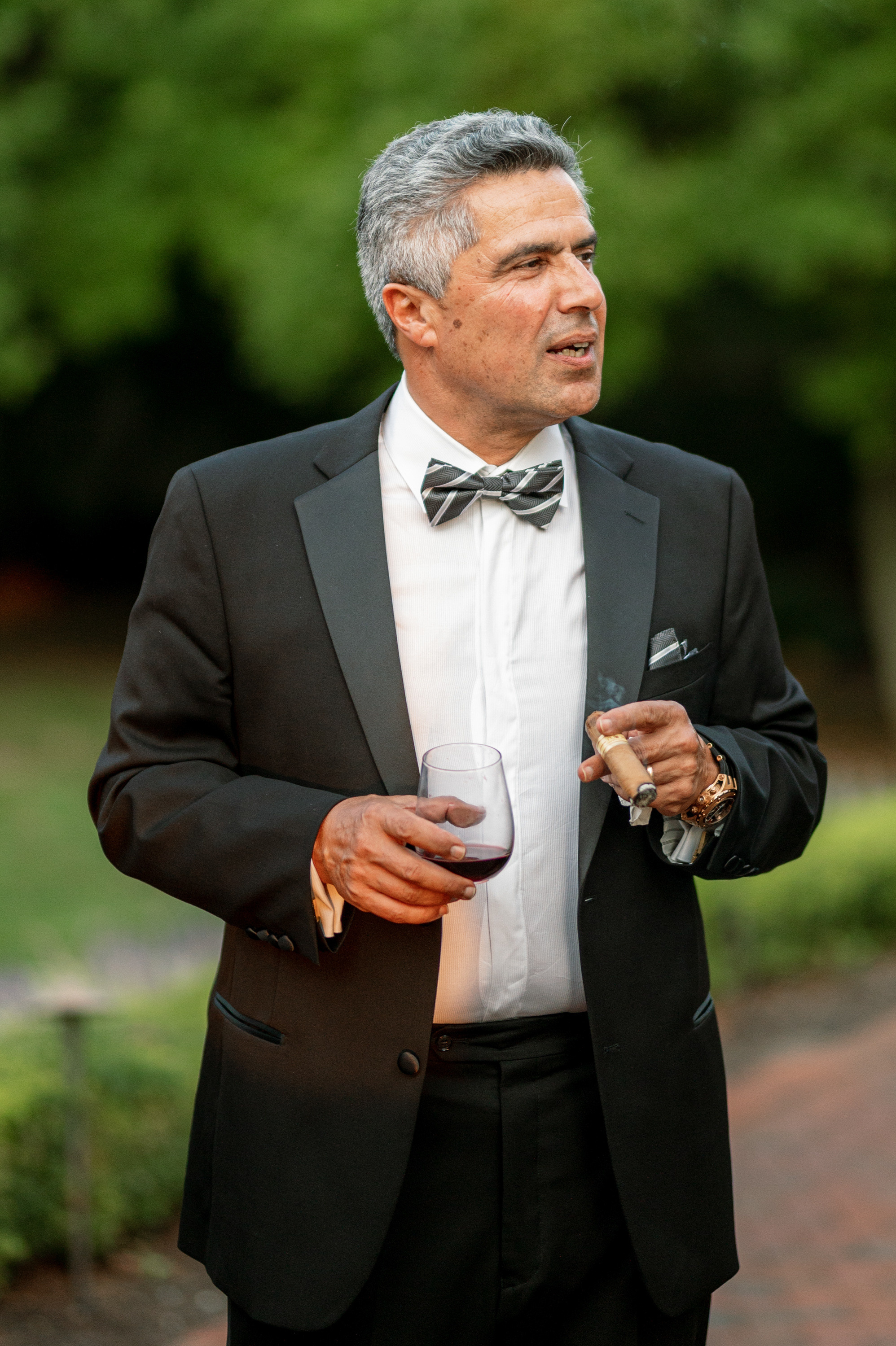 a man in a tuxed suit and bow tie holding a glass of wine