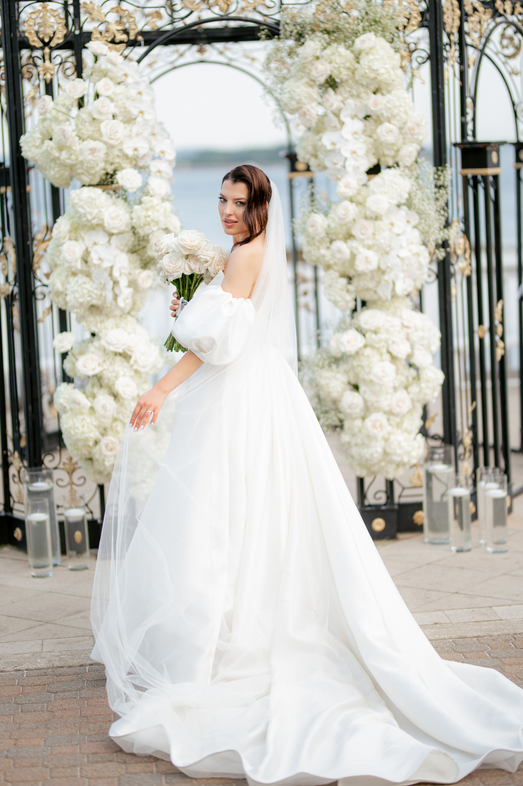 a bride in a white gown standing under an arch of flowers